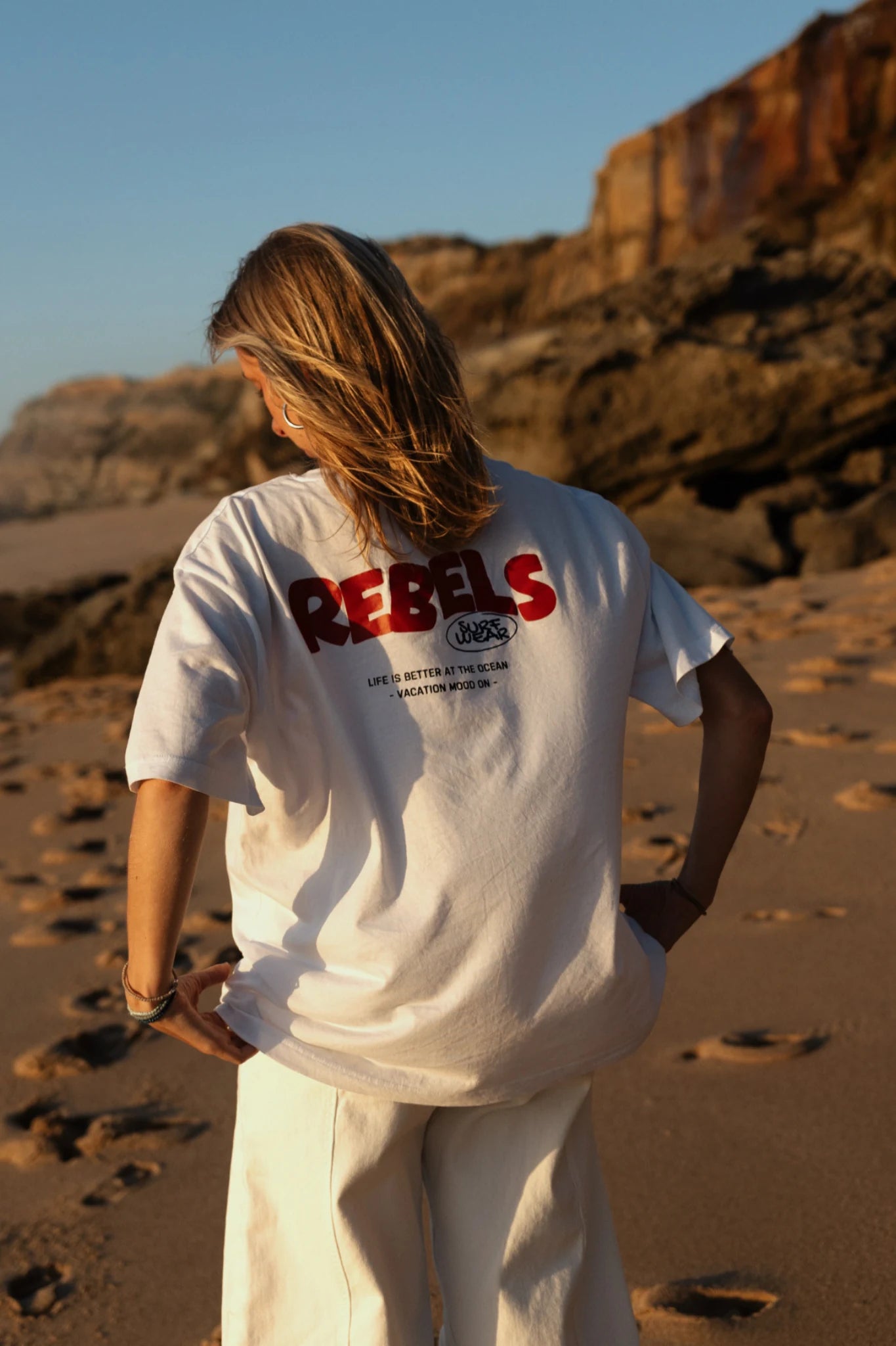 Frau läuft am Strand mit Rebels Surf Wear Light T-Shirt White bei Sonnenuntergang