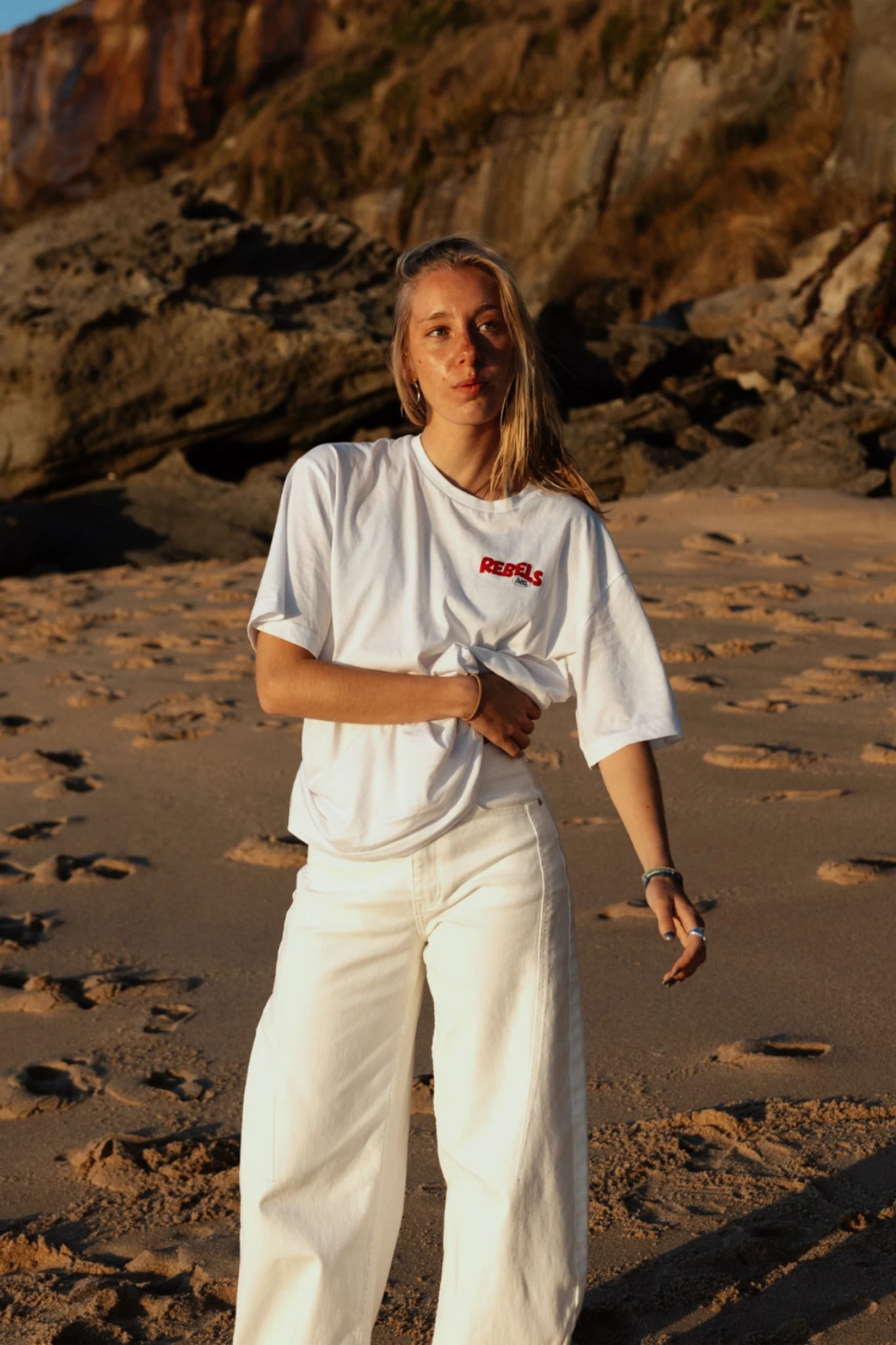 Frau trägt Rebels Surf Wear Light T-Shirt White am Strand bei Sonnenuntergan