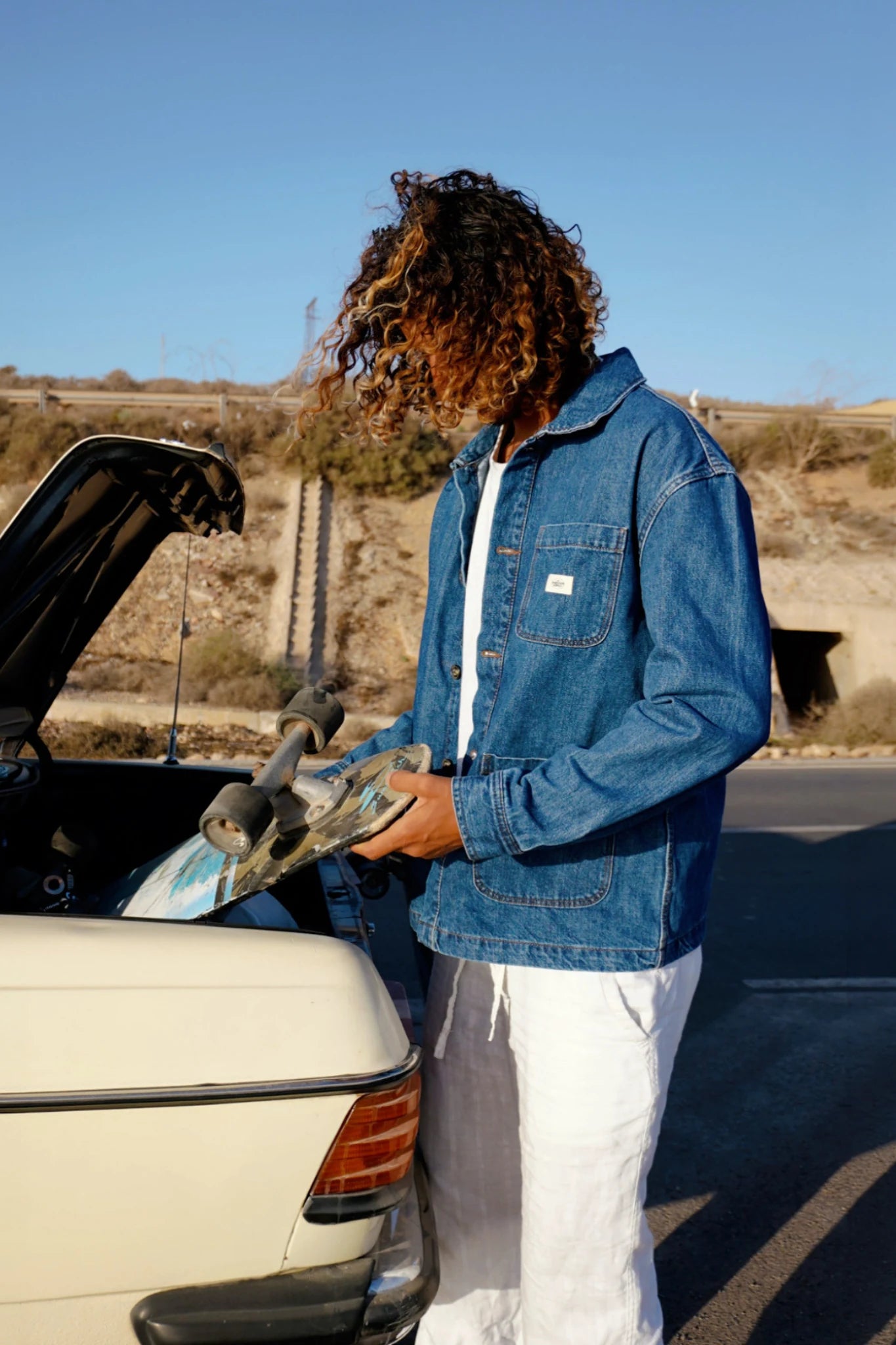 Model trägt blaue Rebels Vintage Denim Jacket 10 Year Fade neben Auto