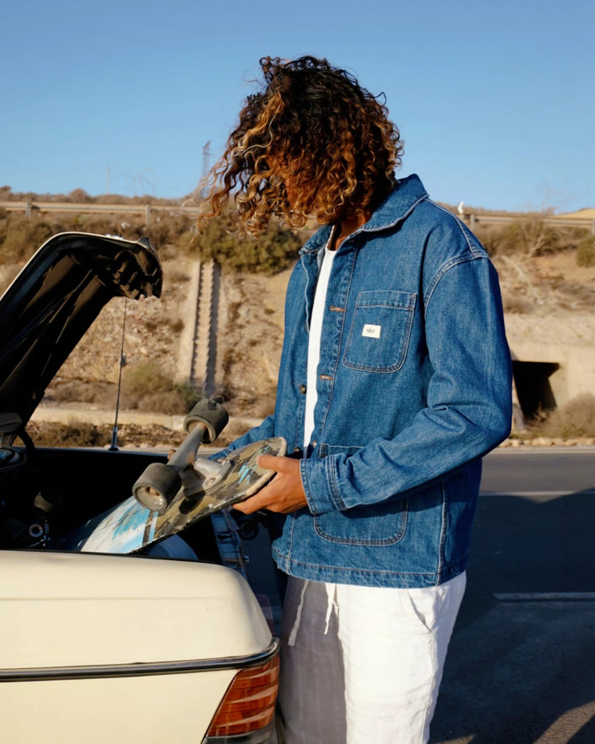 Model trägt blaue Rebels Vintage Denim Jacket 10 Year Fade neben Auto