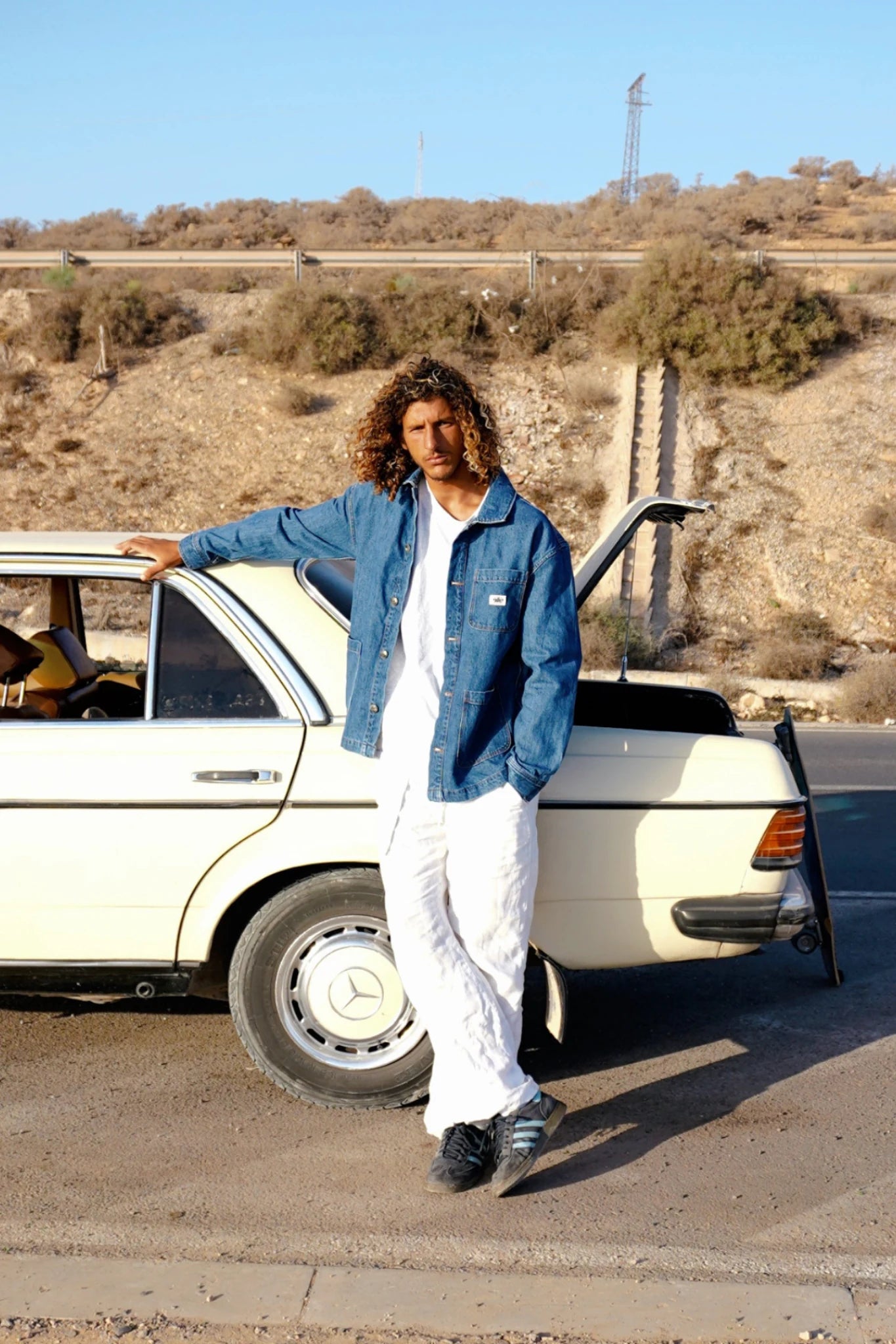 Herren trägt Rebels Vintage Denim Jacket 10 Year Fade mit Skateboard am Auto