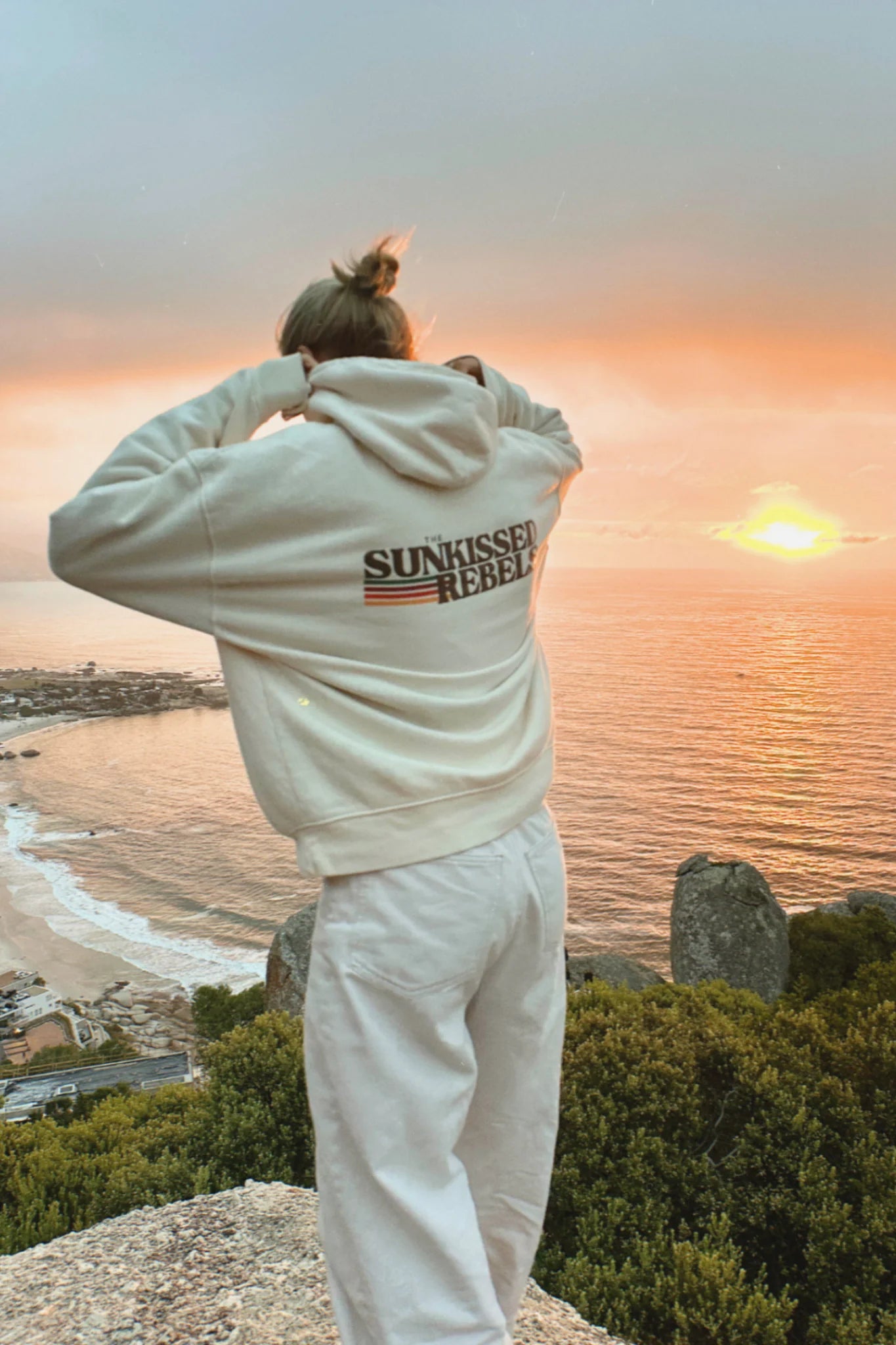 Rückenansicht des Retro Vibes Hoodie Cream von The Sunkissed Rebels bei Sonnenuntergang über dem Meer