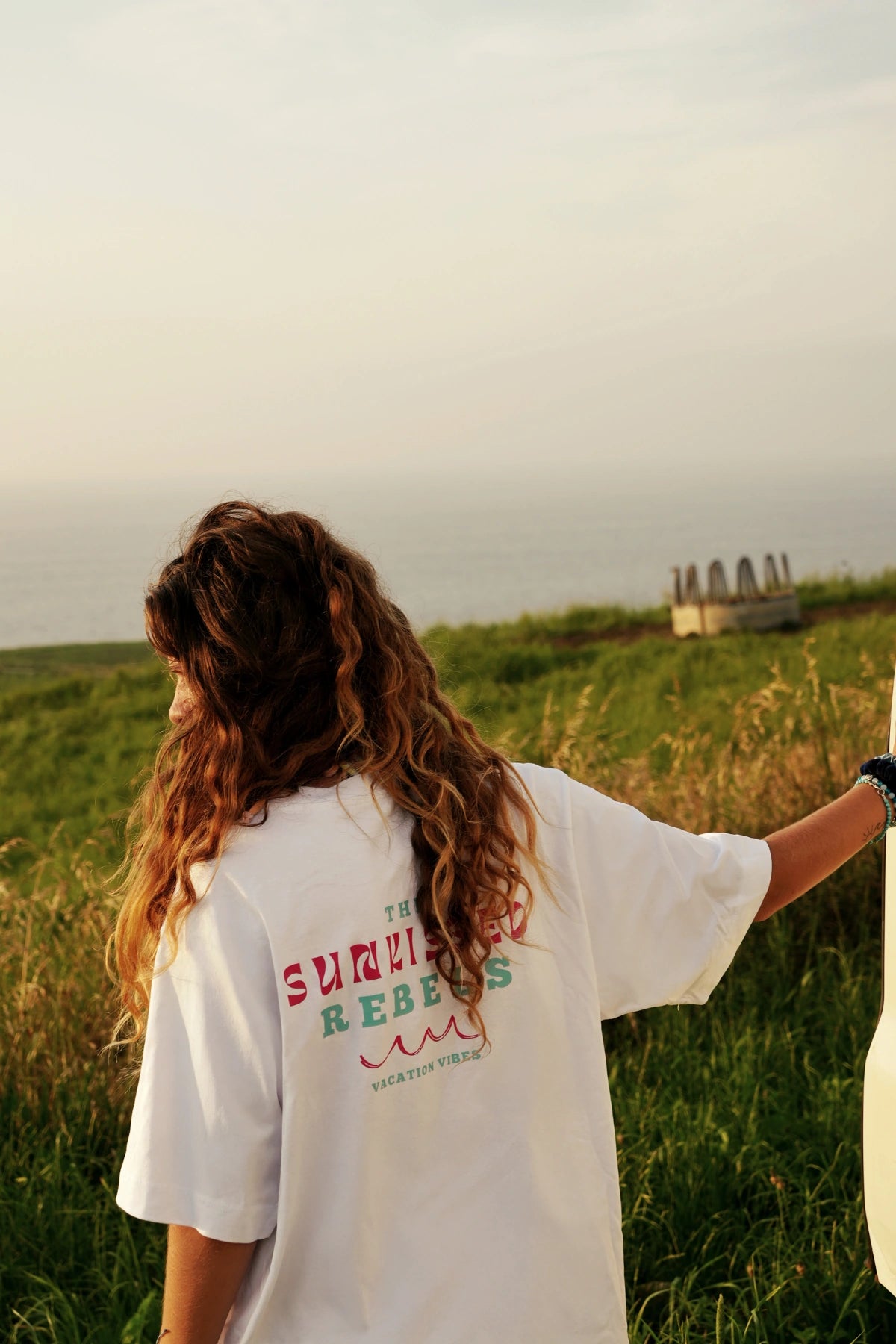 Rückenansicht des weißen Vacation Vibes Shirts mit Print vor idyllischer Meerkulisse