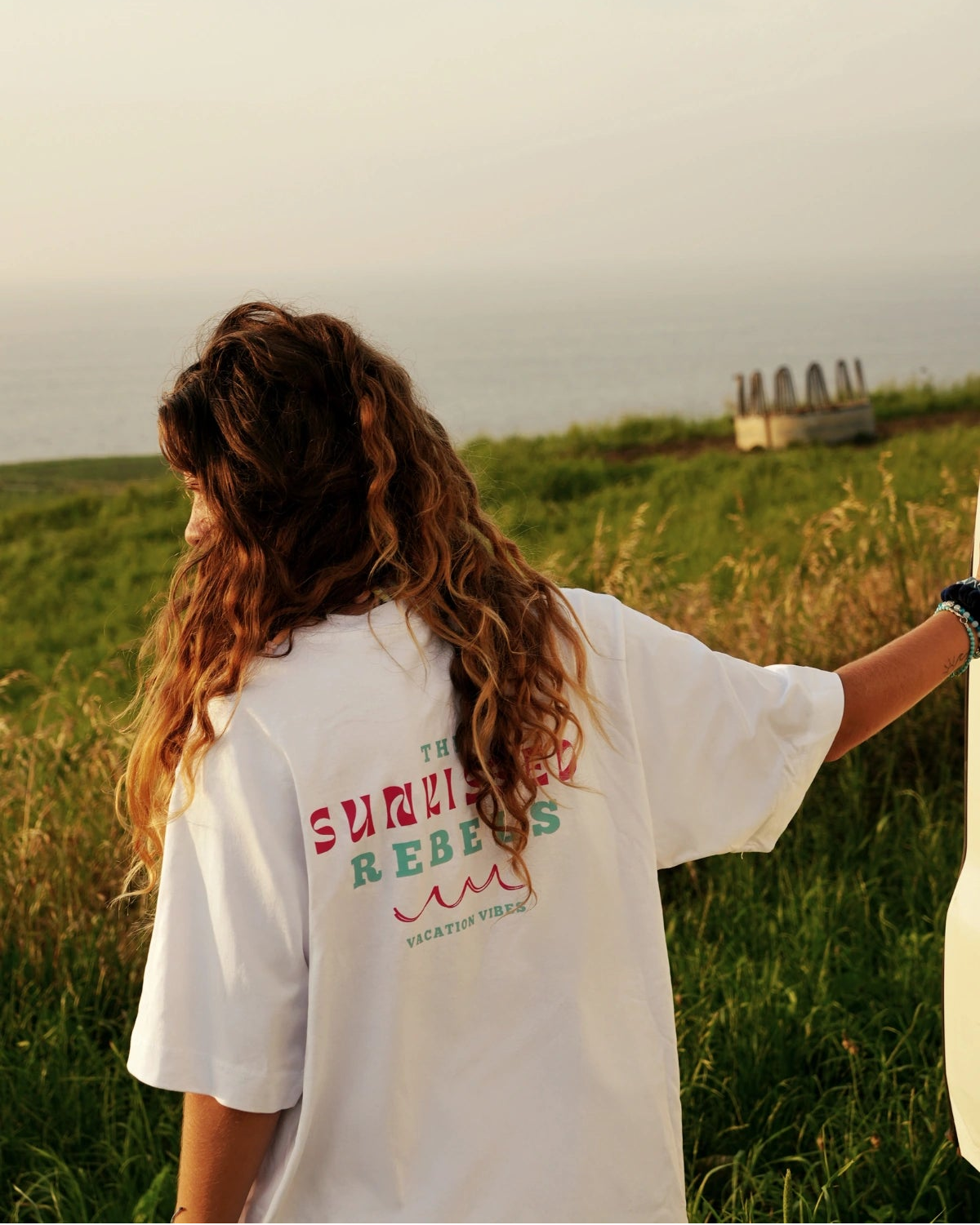 Rückenansicht des weißen Vacation Vibes Shirts mit Print vor idyllischer Meerkulisse