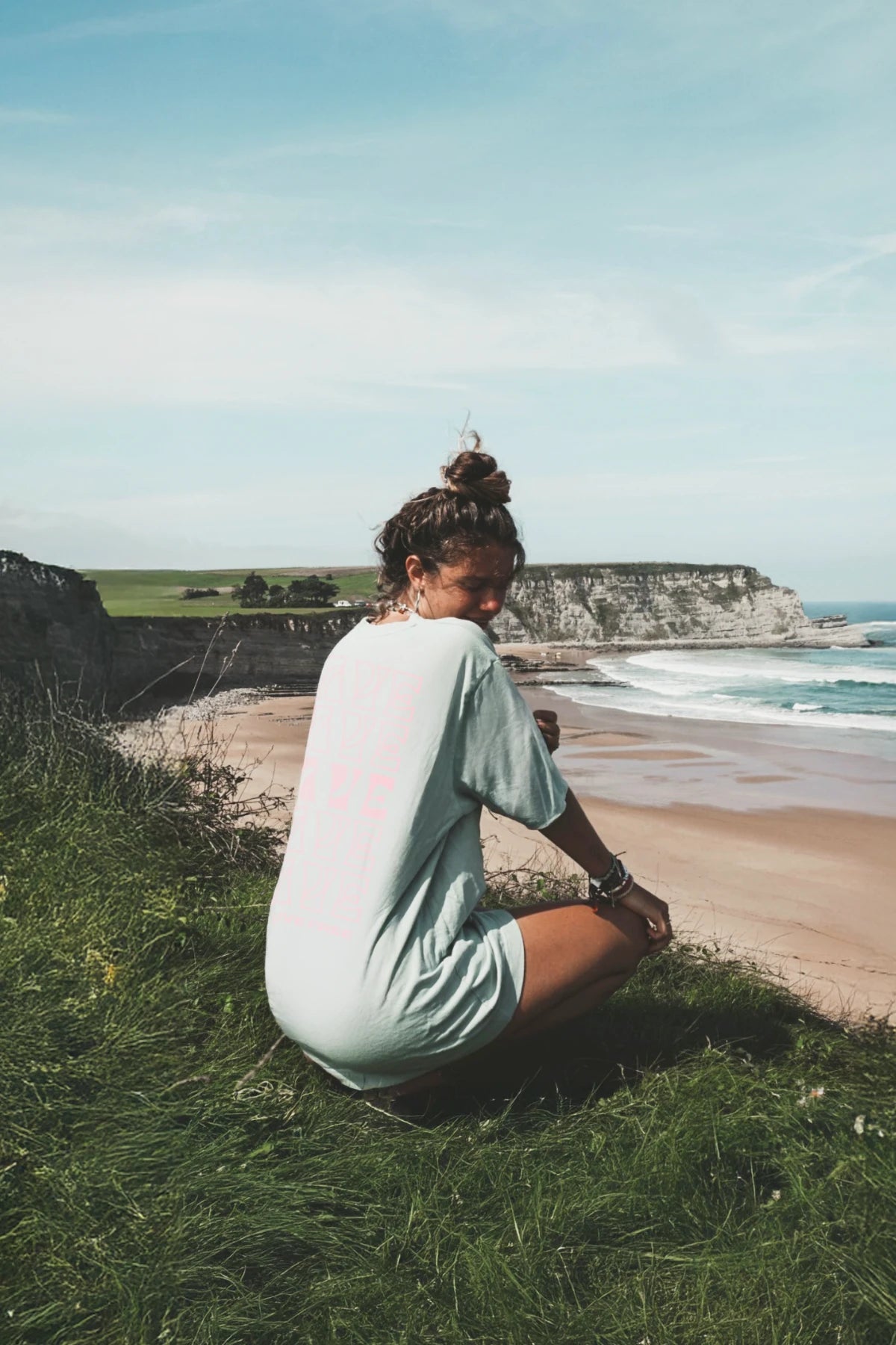 he Sunkissed Rebels T-Shirt „Live Free“ – Rückansicht beim Ausruhen auf Klippe