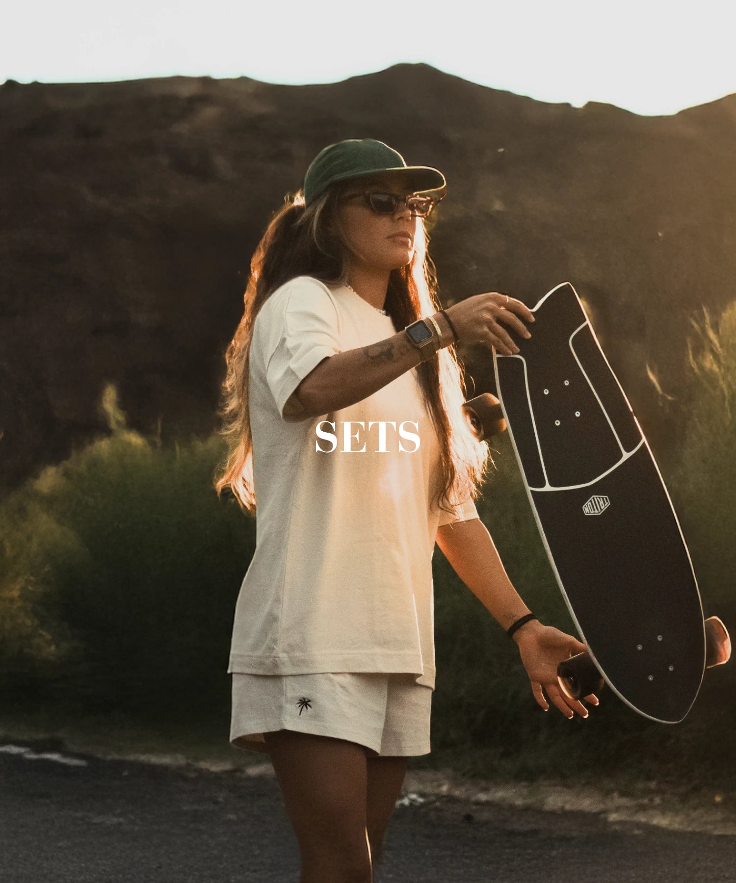 Frau im urbanen Skater-Look bei Sonnenuntergang mit Longboard und lässigem Sommer-Set-Outfit