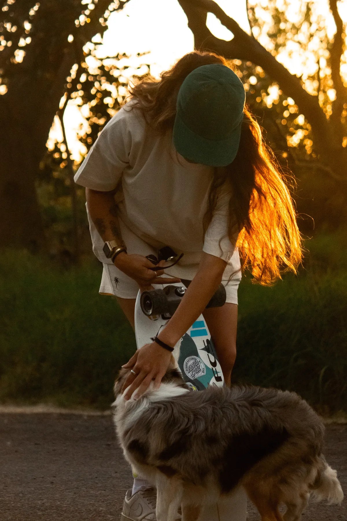 Frau mit Skateboard und Hund in der Abendsonne, naturfarbenes T-Shirt
