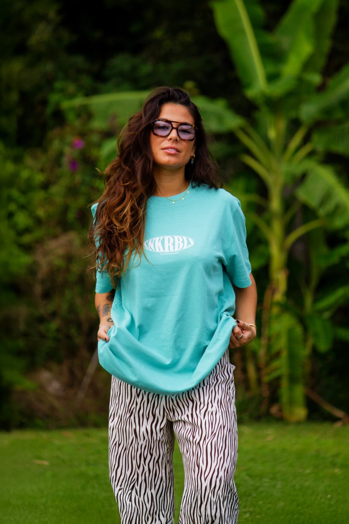 SNKRBLS T-Shirt in Pool Blue getragen im Garten mit lässigem Styling und tropischem Hintergrund