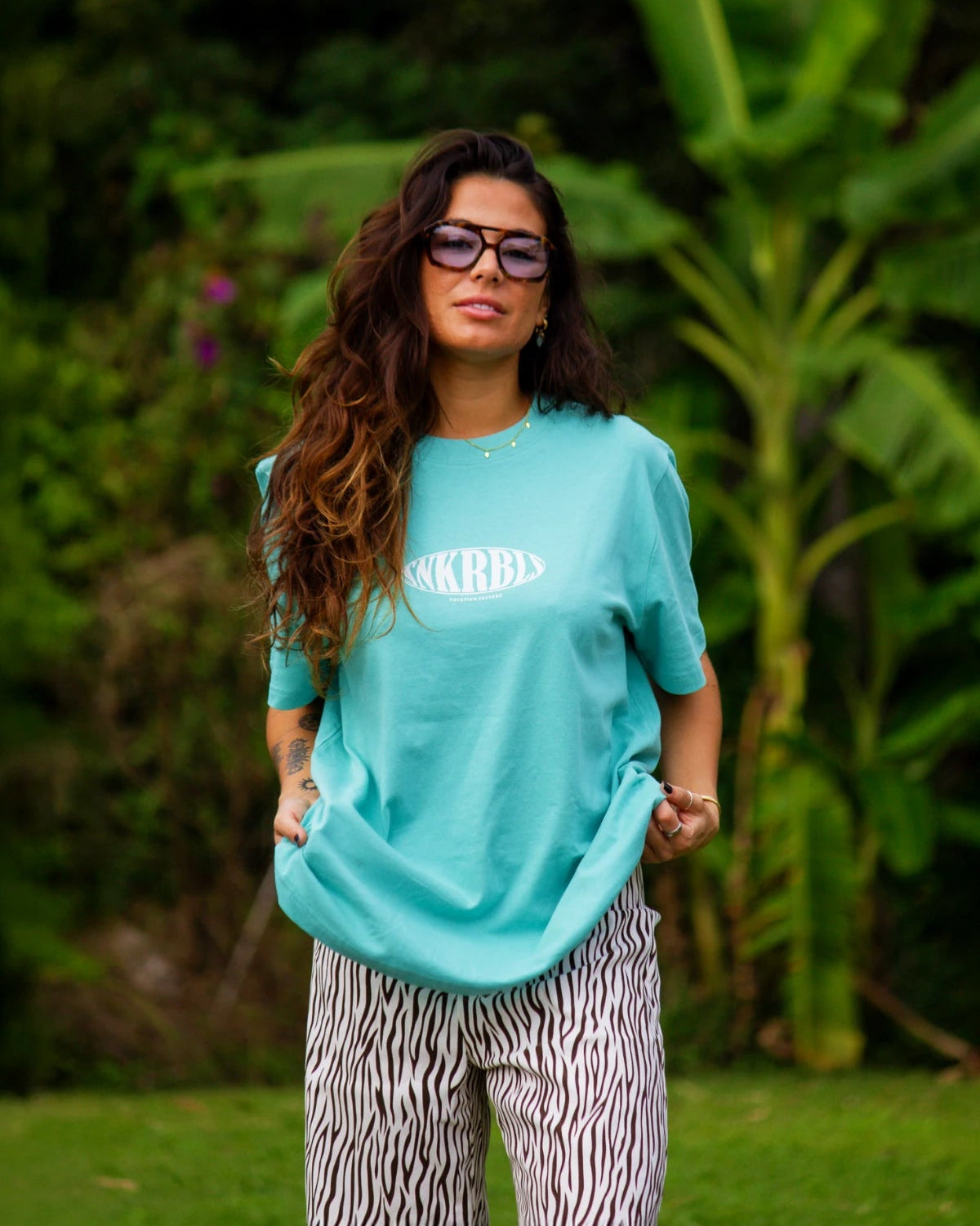 SNKRBLS T-Shirt in Pool Blue getragen im Garten mit lässigem Styling und tropischem Hintergrund