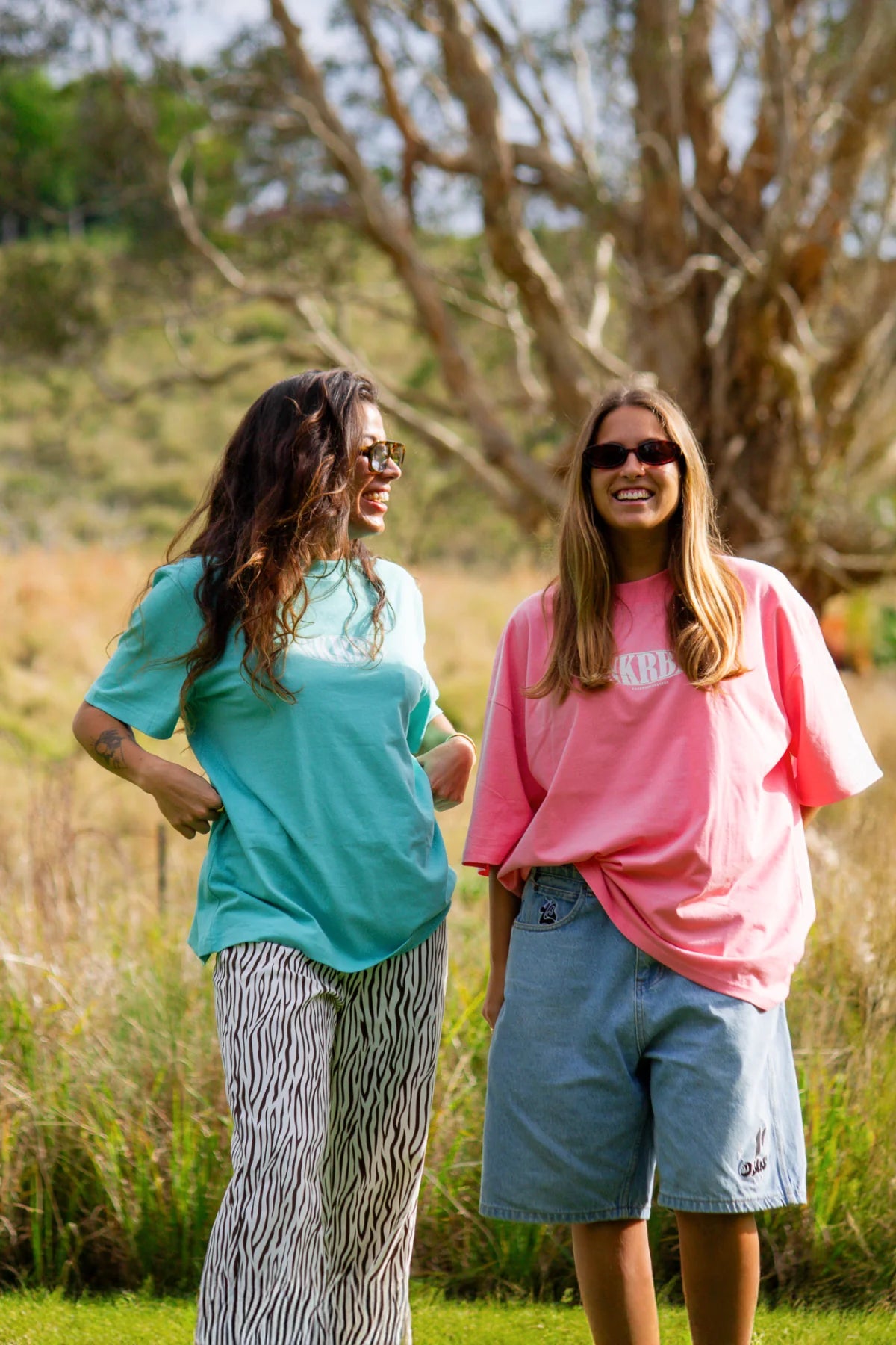 Zwei Freundinnen tragen SNKRBLS T-Shirts im Sommer-Look unter strahlender Sonne