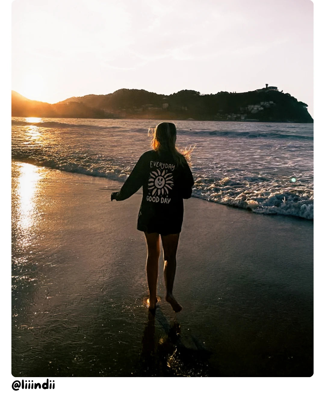 Model von The Sunkissed Rebels läuft während des Sonnenuntergangs am Strand entlang und trägt einen Sweater mit Rückenprint.