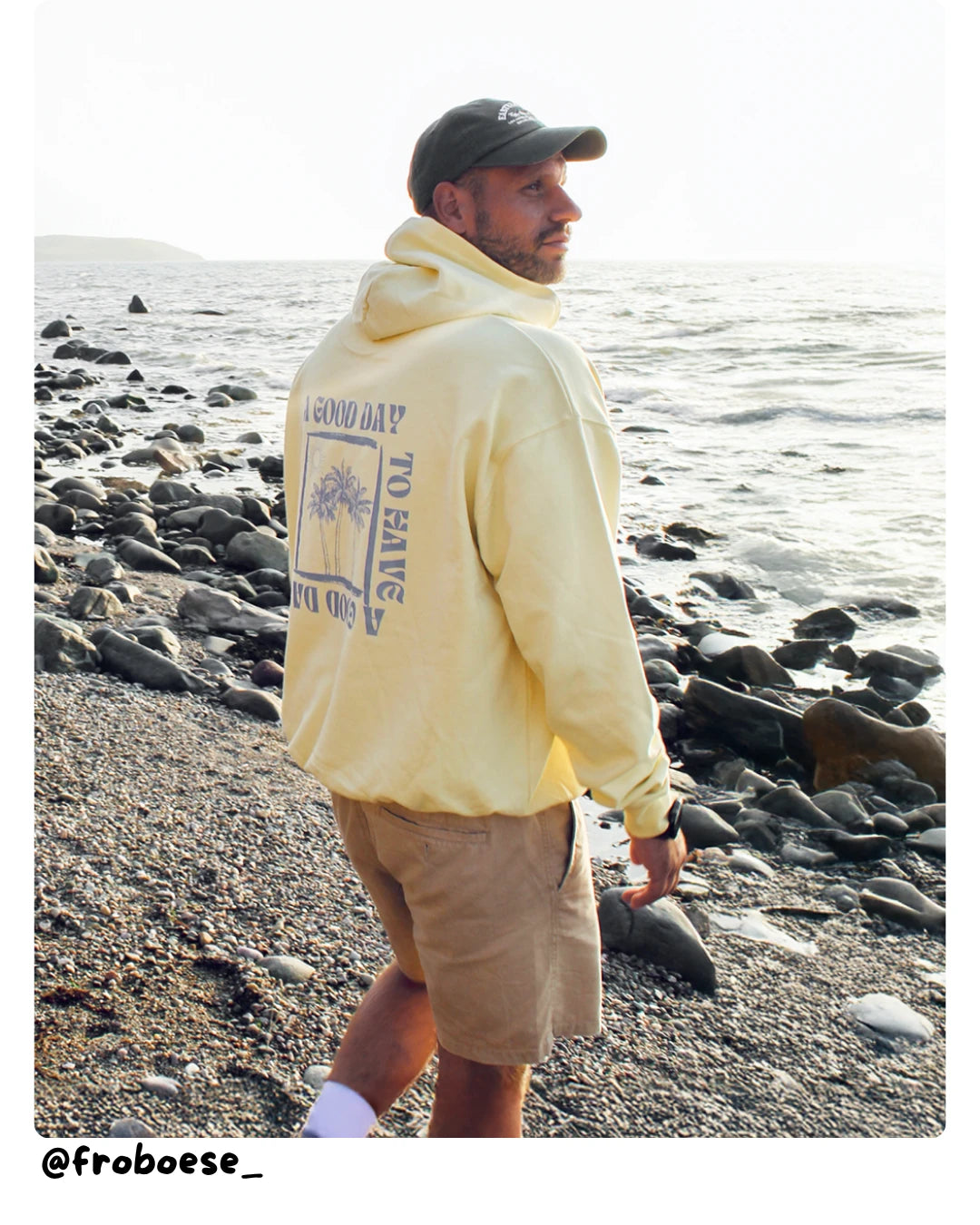 Model von The Sunkissed Rebels läuft während des Sonnenuntergangs am Strand entlang und trägt einen Hoodie mit Rückenprint.