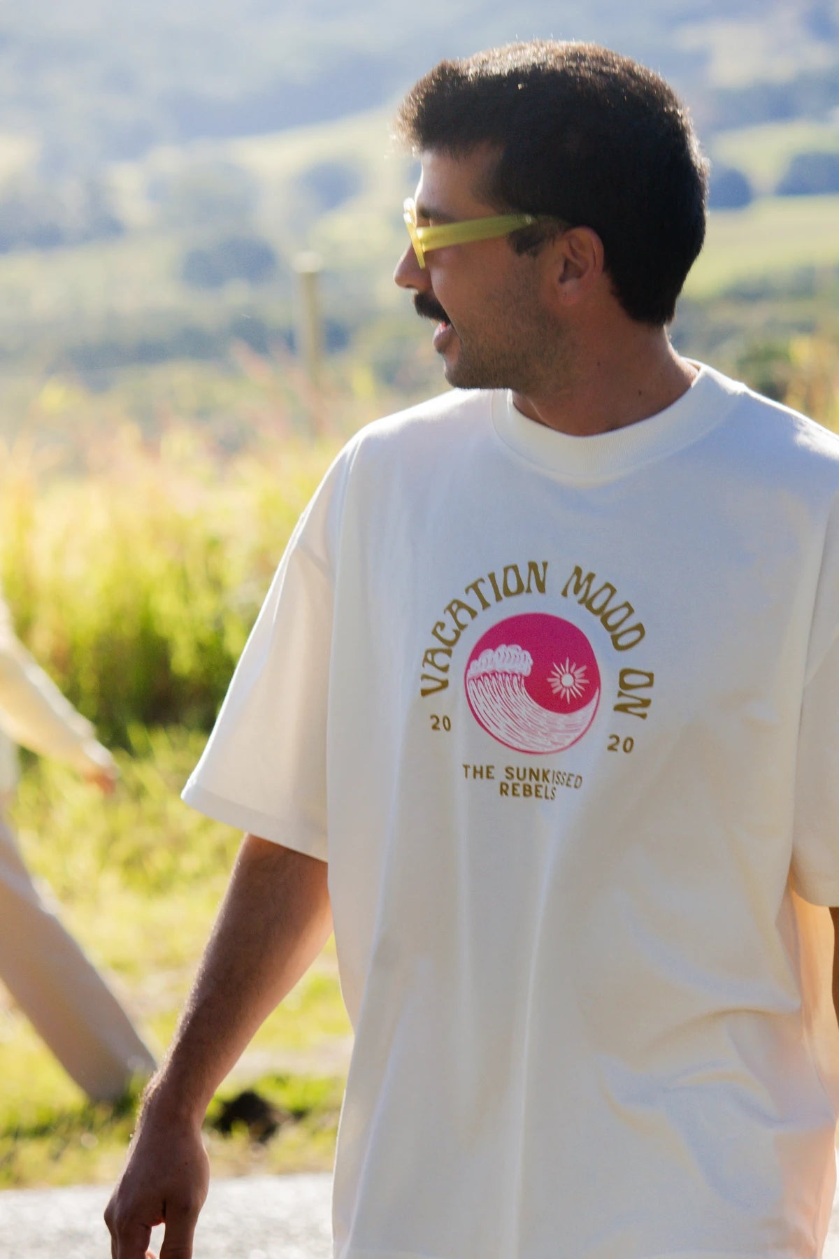 Mann mit Sonnenbrille trägt das Vacation Mood On T-Shirt in Cream bei strahlendem Sonnenschein – lässiger Skater-Style