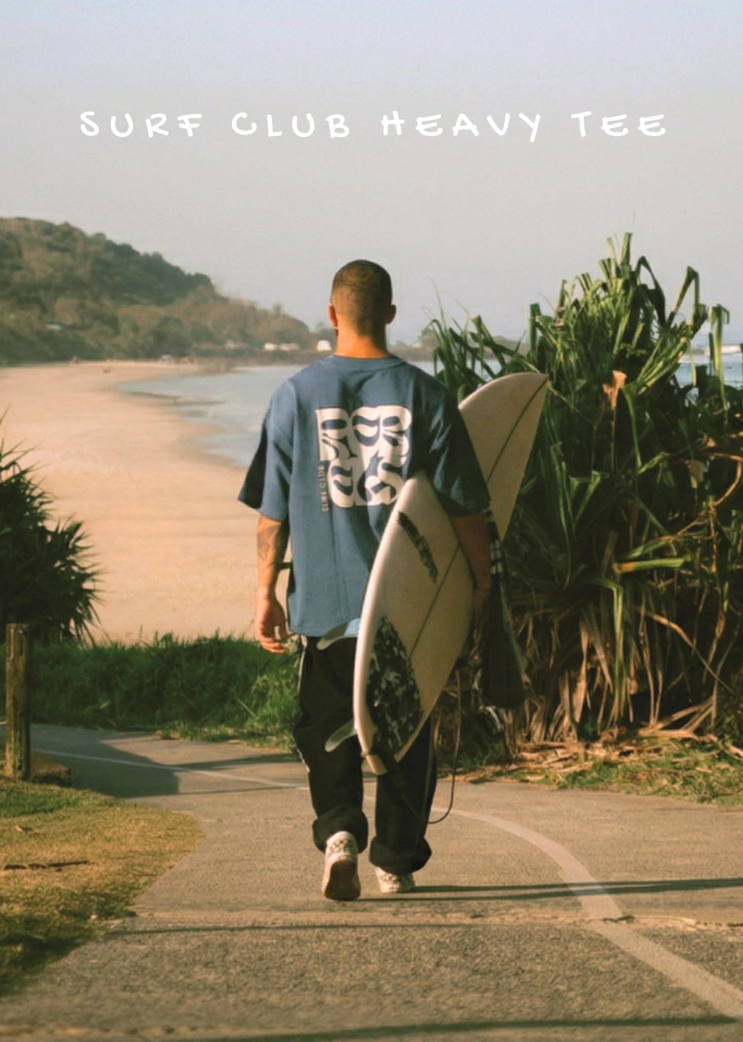 Surfer läuft Richtung Strand mit Surfboard und trägt Surf Club Heavy Tee von The Sunkissed Rebels