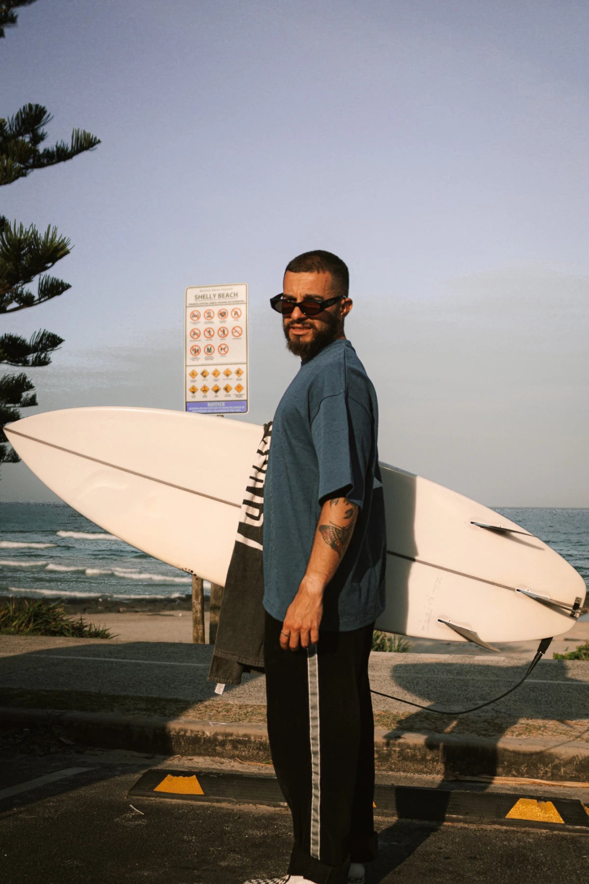 Surf Club Heavy T-Shirt – Deep Blue von The Sunkissed Rebels, getragen beim Spaziergang entlang der Küste – modernes Surf Outfit für Herren.