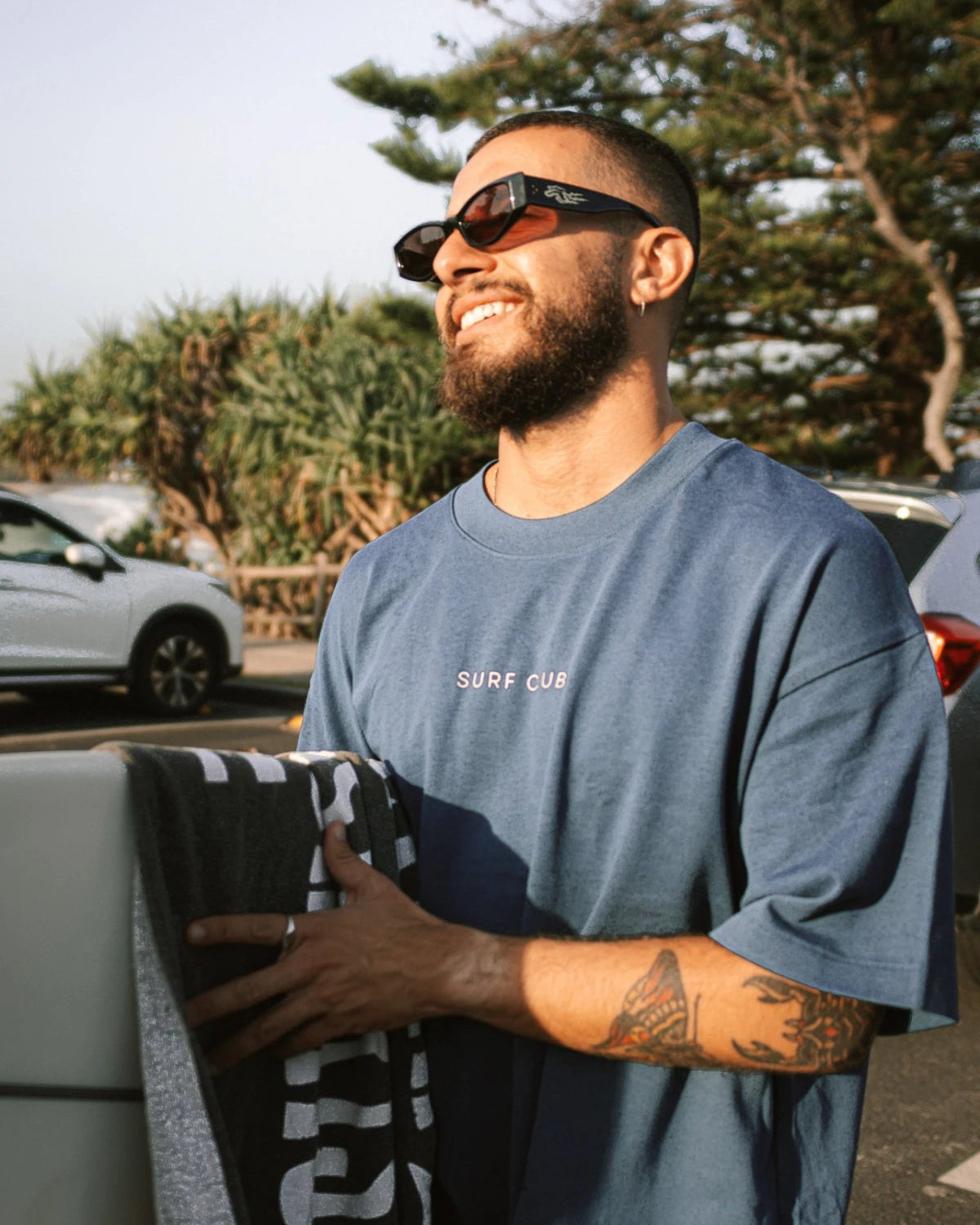 Entspannter Look am Surfspot – Surf Club Heavy T-Shirt Deep Blue von The Sunkissed Rebels mit Surfbrett, perfektes Outfit für Strandtage.