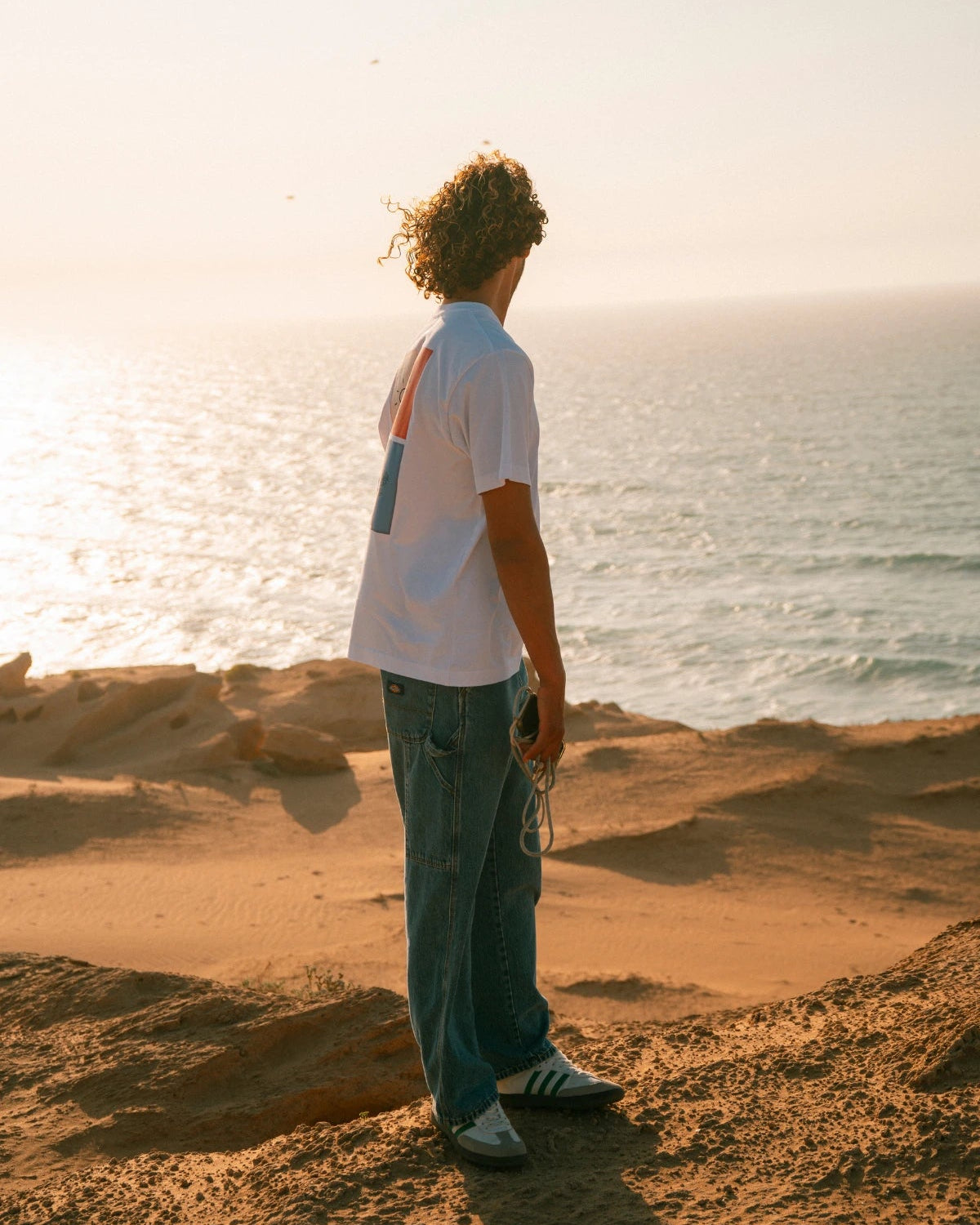 The Rebel Elements T-Shirt White Seitenansicht Backprint getragen am Meer minimalistisches Design