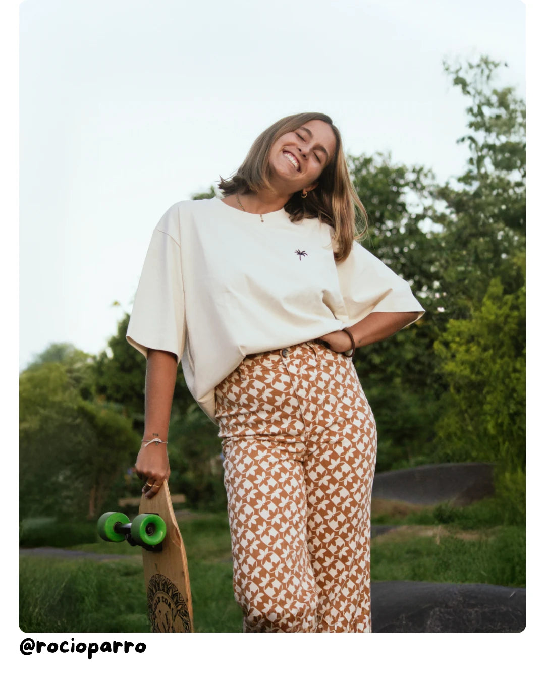 Model von The Sunkissed Rebel trägt ein creamfarbenes T-Shirt vor Palmen und warmer Atmosphäre.
