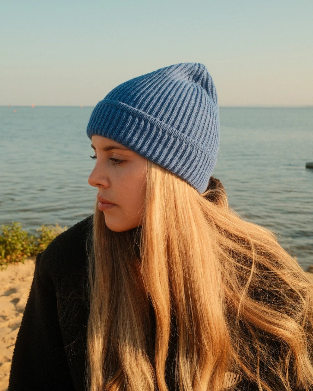 Gerippte blaue Beanie Rebels Knit Beanie Ocean Blue von The Sunkissed Rebels in Seitenansicht am Wasser.