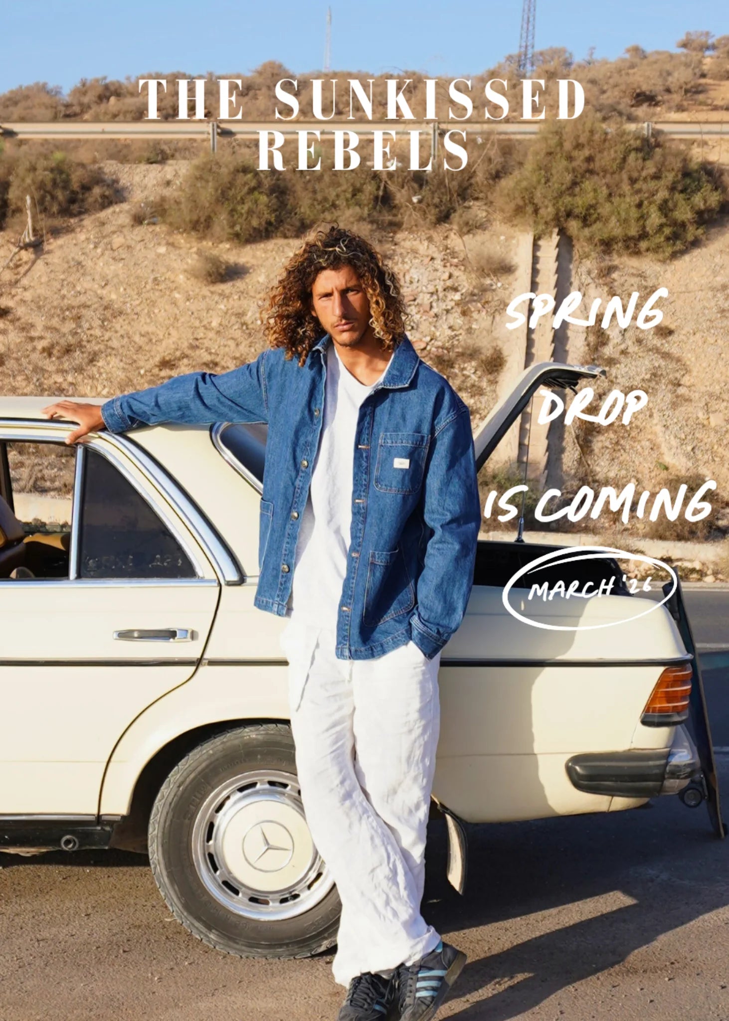 The Sunkissed Rebels Spring Drop 2026 – Model im nachhaltigen Vintage Denim Jacket neben klassischem Oldtimer in sonniger Wüstenkulisse (Campaign Hochformat)