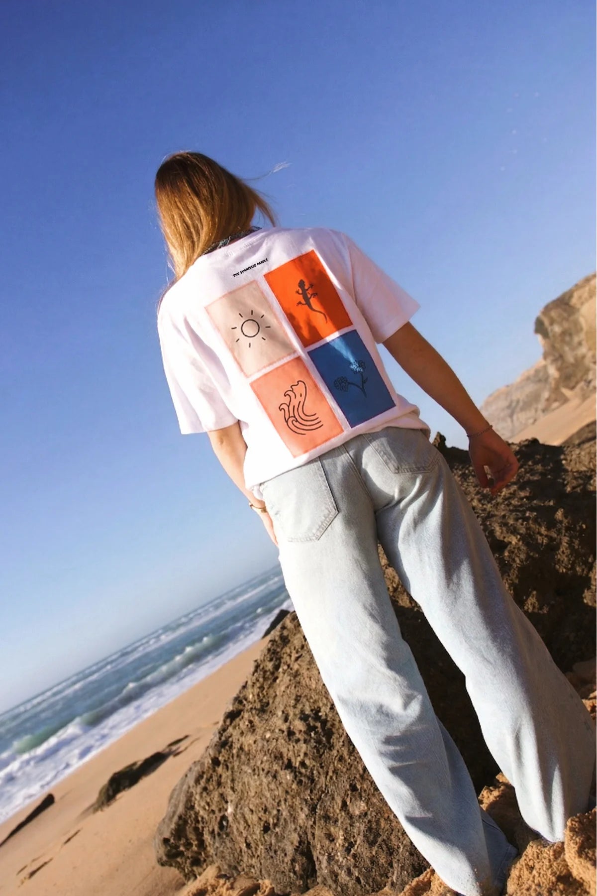 Perspektivische Aufnahme des The Sunkissed Rebels T-Shirts in Weiß; zeigt das farbenfrohe Grafik-Design auf dem Rücken in hochwertiger Druckqualität.