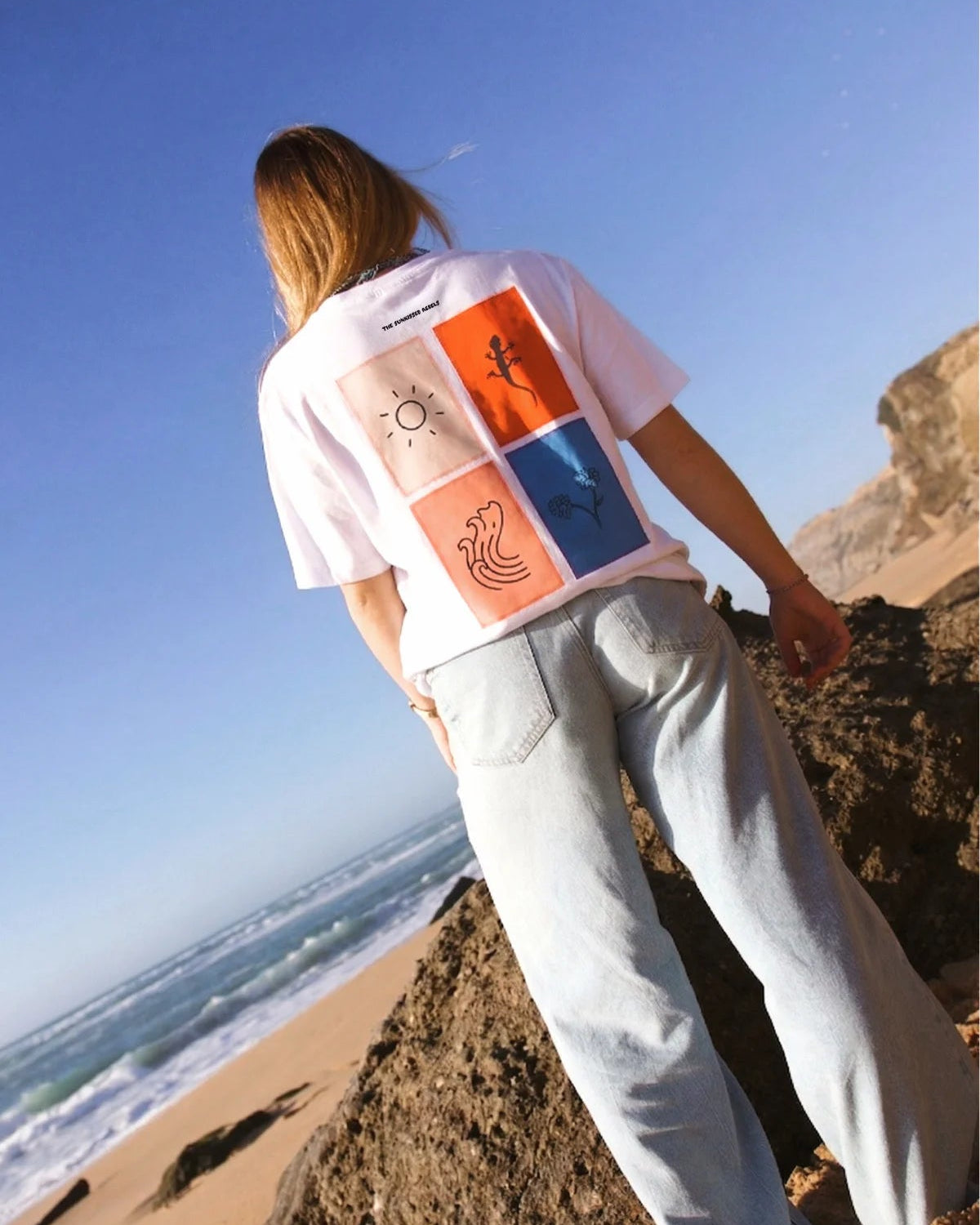 Perspektivische Aufnahme des The Sunkissed Rebels T-Shirts in Weiß; zeigt das farbenfrohe Grafik-Design auf dem Rücken in hochwertiger Druckqualität.