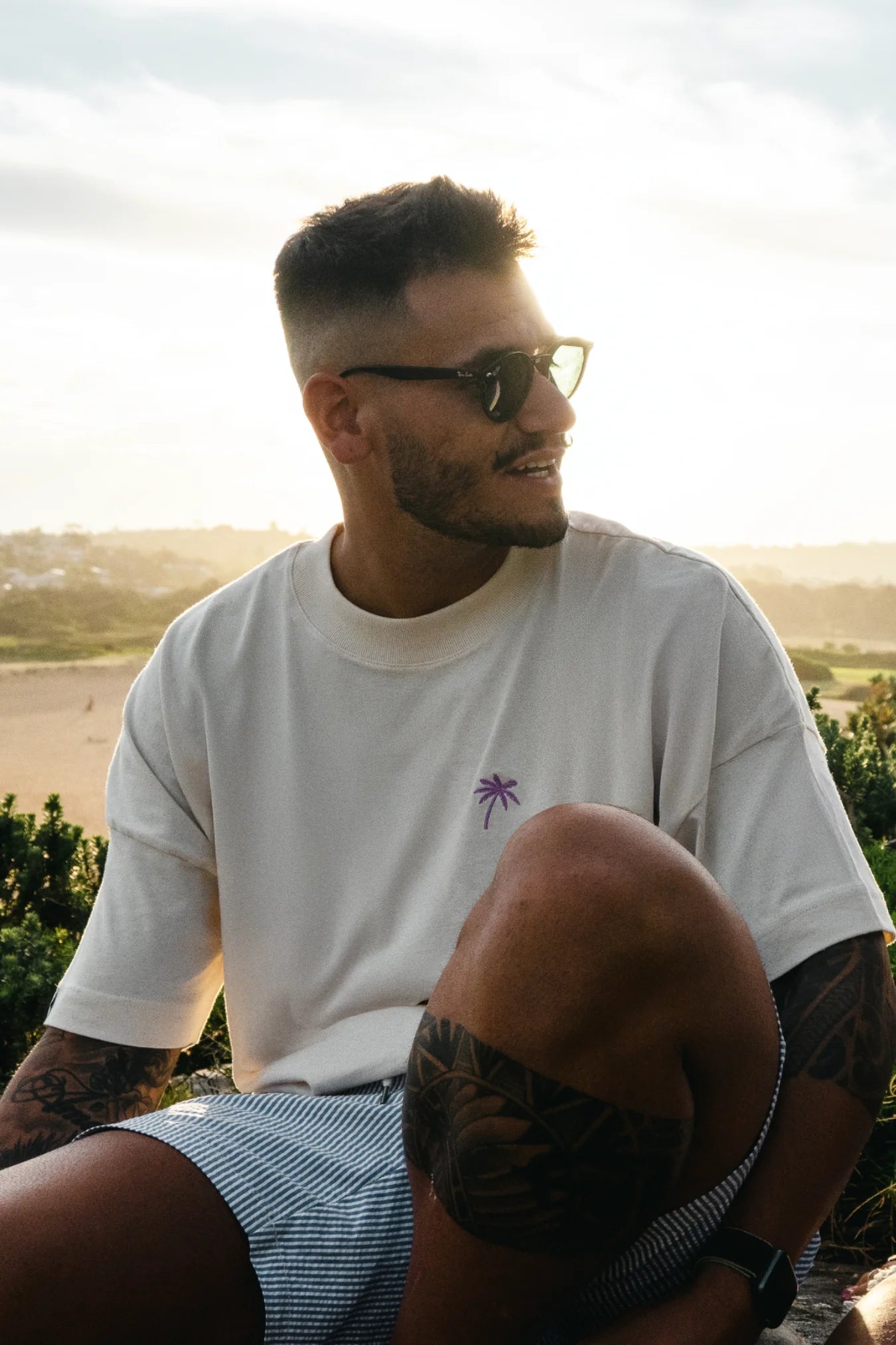 Lachender Mann trägt Oversized T-Shirt mit Palmenstick – Naturtal Raw Stoff im Tageslicht