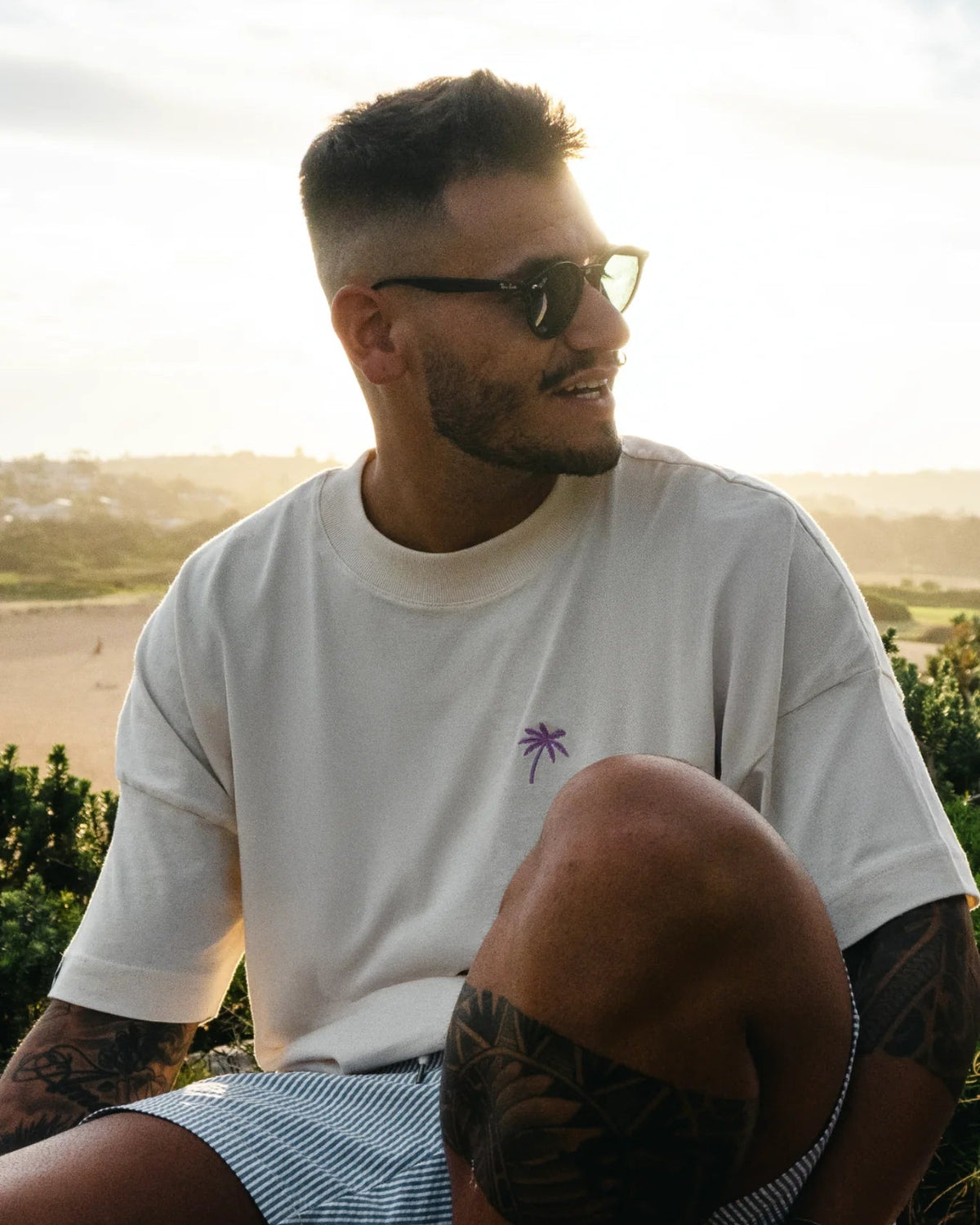 Lachender Mann trägt Oversized T-Shirt mit Palmenstick – Naturtal Raw Stoff im Tageslicht