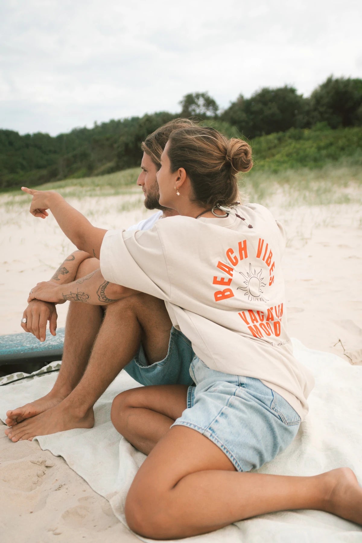 Paar am Strand in T-Shirts von The Sunkissed Rebels – Beachvibes in Sand und Weiß
