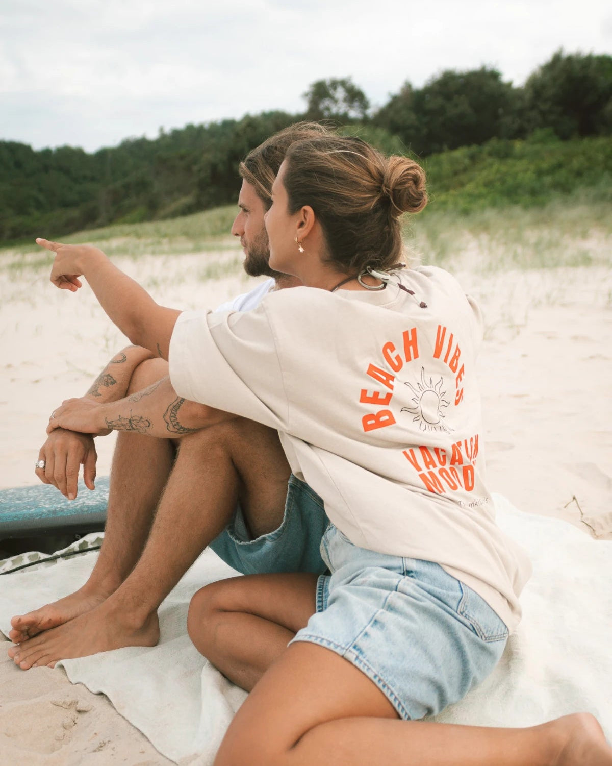 Paar am Strand in T-Shirts von The Sunkissed Rebels – Beachvibes in Sand und Weiß