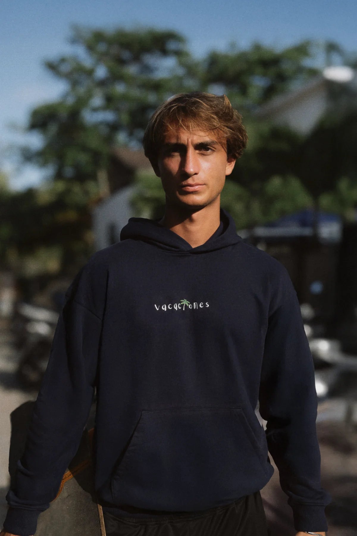 Mann trägt den Vacaciones Oversized Hoodie in Dark Ocean auf der Straße, sonniges Urlaubs-Feeling.