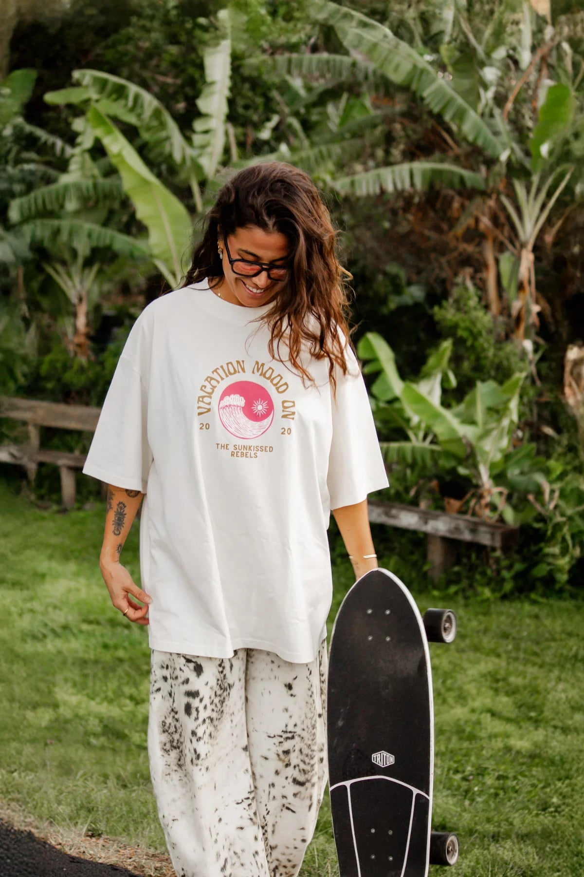 Skaterin mit "Vacation Mood On" T-Shirt in Cremeweiß vor tropischem Hintergrund