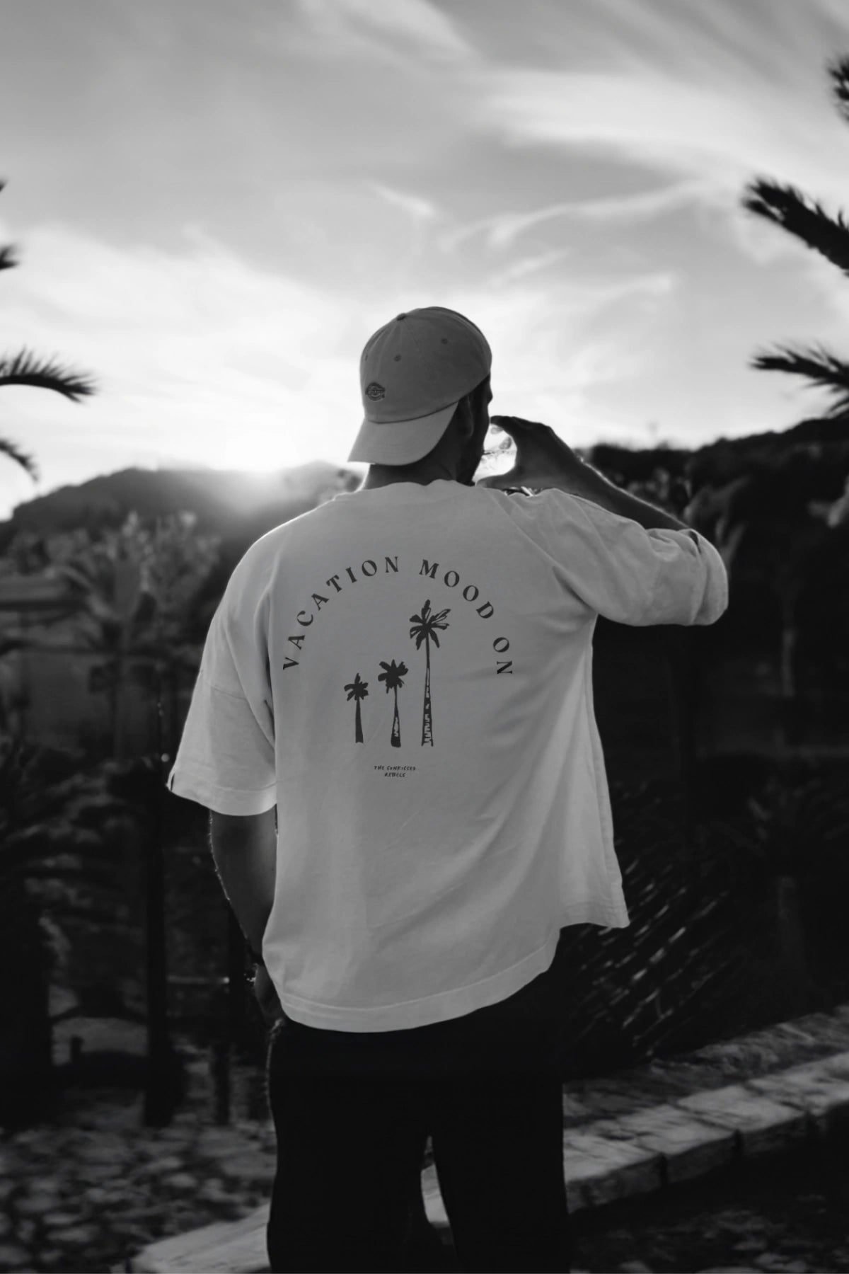 Mann mit weißem 'Vacation Mood On' Oversized T-Shirt in weiß. Aufnahme bei Sonnenuntergang