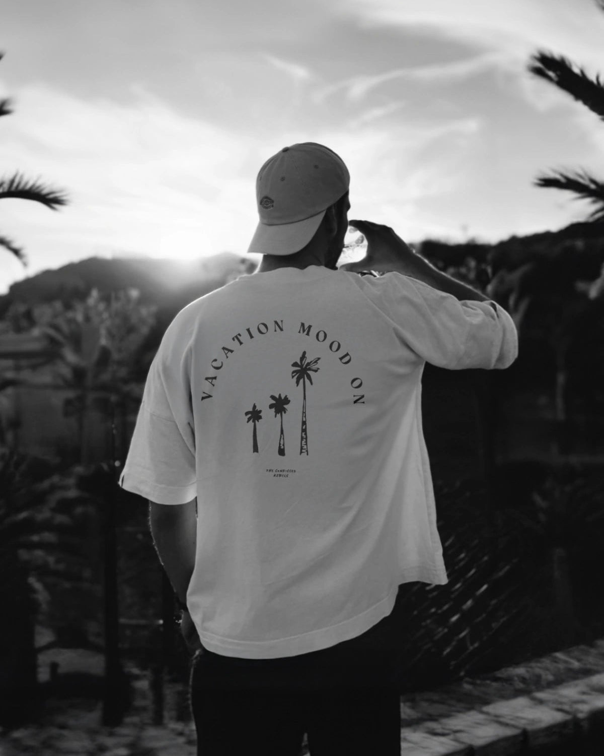 Mann mit weißem 'Vacation Mood On' Oversized T-Shirt in weiß. Aufnahme bei Sonnenuntergang