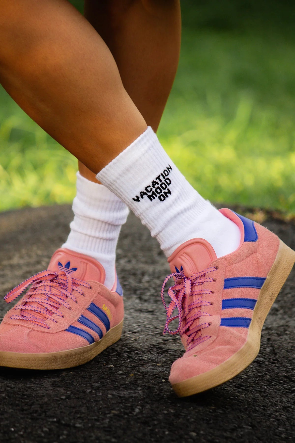 Nahaufnahme der weißen "Vacation Mood On" Socken kombiniert mit rosa Adidas Gazelle Sneakern