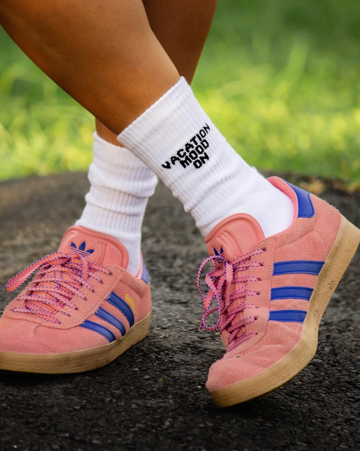 Nahaufnahme der weißen "Vacation Mood On" Socken kombiniert mit rosa Adidas Gazelle Sneakern