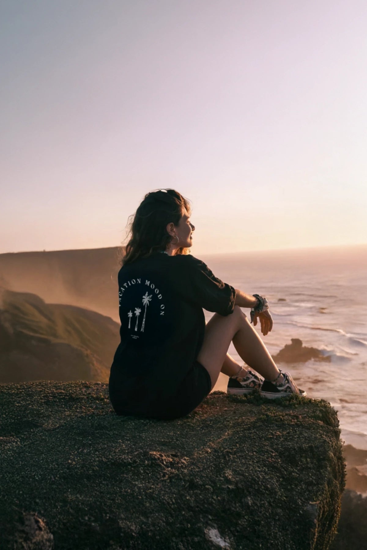 Frau trägt Vacation Mood On T-Shirt am Felsen mit Sonnenuntergang im Hintergrund