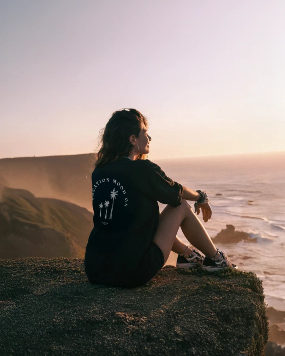 Frau trägt Vacation Mood On T-Shirt am Felsen mit Sonnenuntergang im Hintergrund