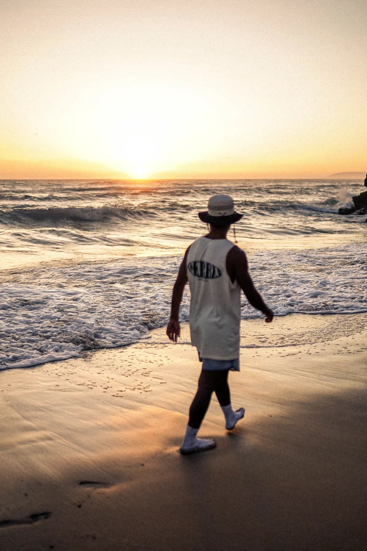 Silhouette eines Mannes im SNKRBLS Tank Top beim Spaziergang am Strand im Sonnenuntergang
