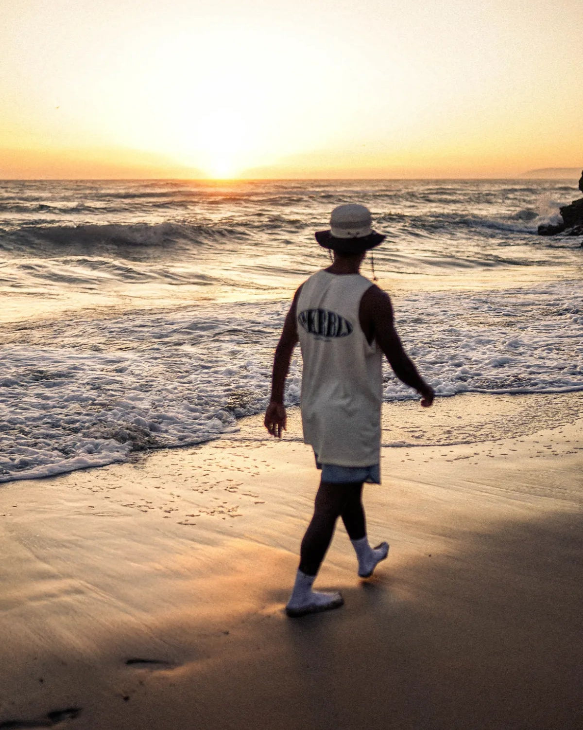 Silhouette eines Mannes im SNKRBLS Tank Top beim Spaziergang am Strand im Sonnenuntergang