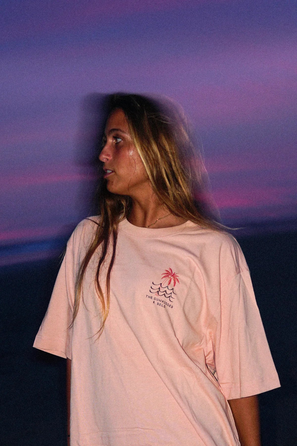 Detailaufnahme des nachhaltigen Waves & Palm Trees Oversized T-Shirts in Coral mit Brust-Print vor einem pink-violetten Abendhimmel.