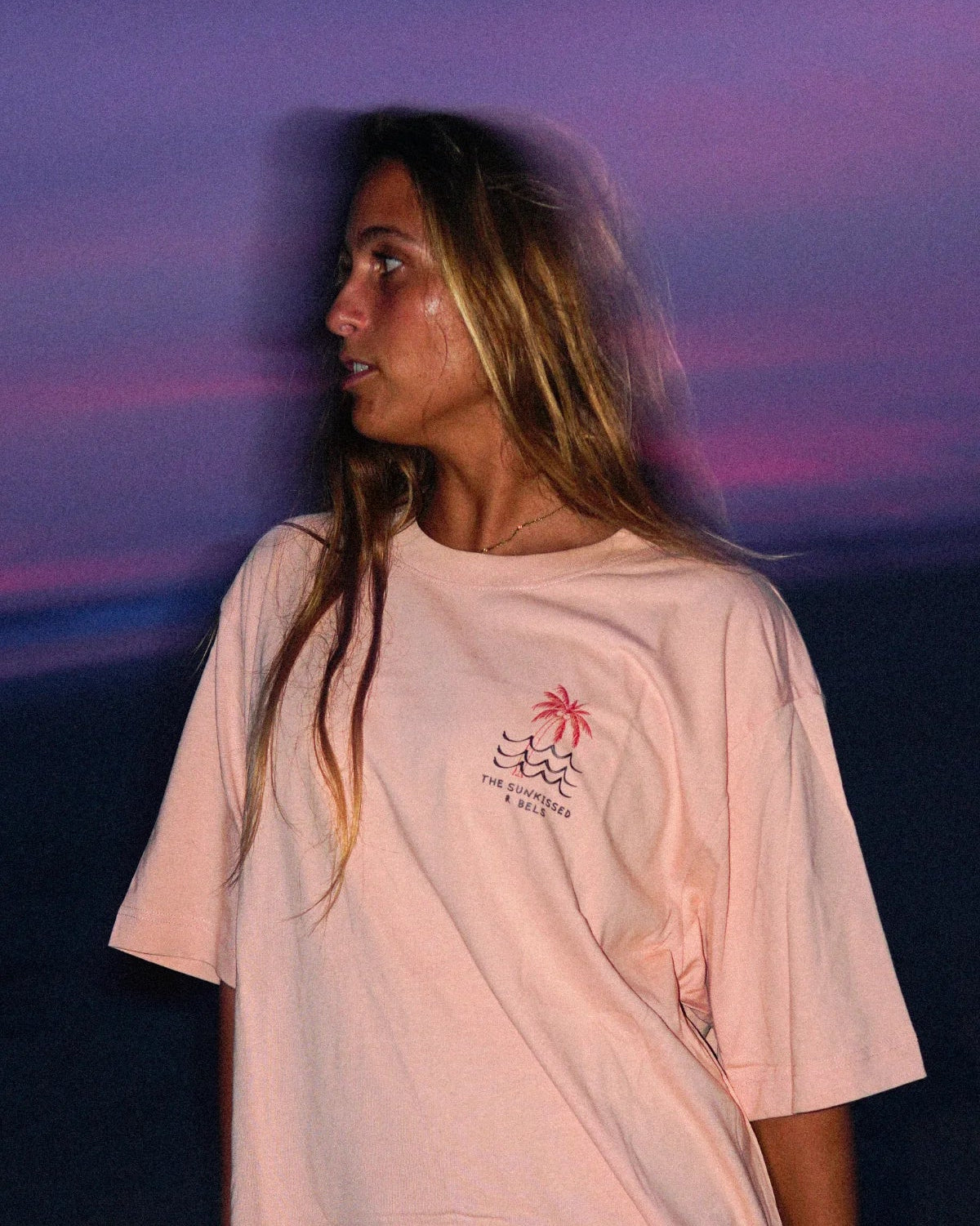 Detailaufnahme des nachhaltigen Waves & Palm Trees Oversized T-Shirts in Coral mit Brust-Print vor einem pink-violetten Abendhimmel.