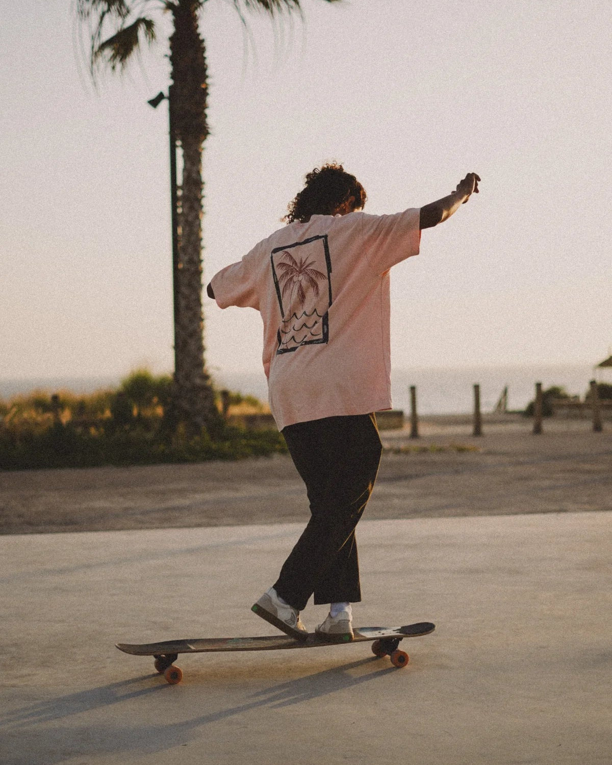 Oversized T-Shirt in Coral beim Skaten – Rückansicht mit Wellen-Print von The Sunkissed Rebels