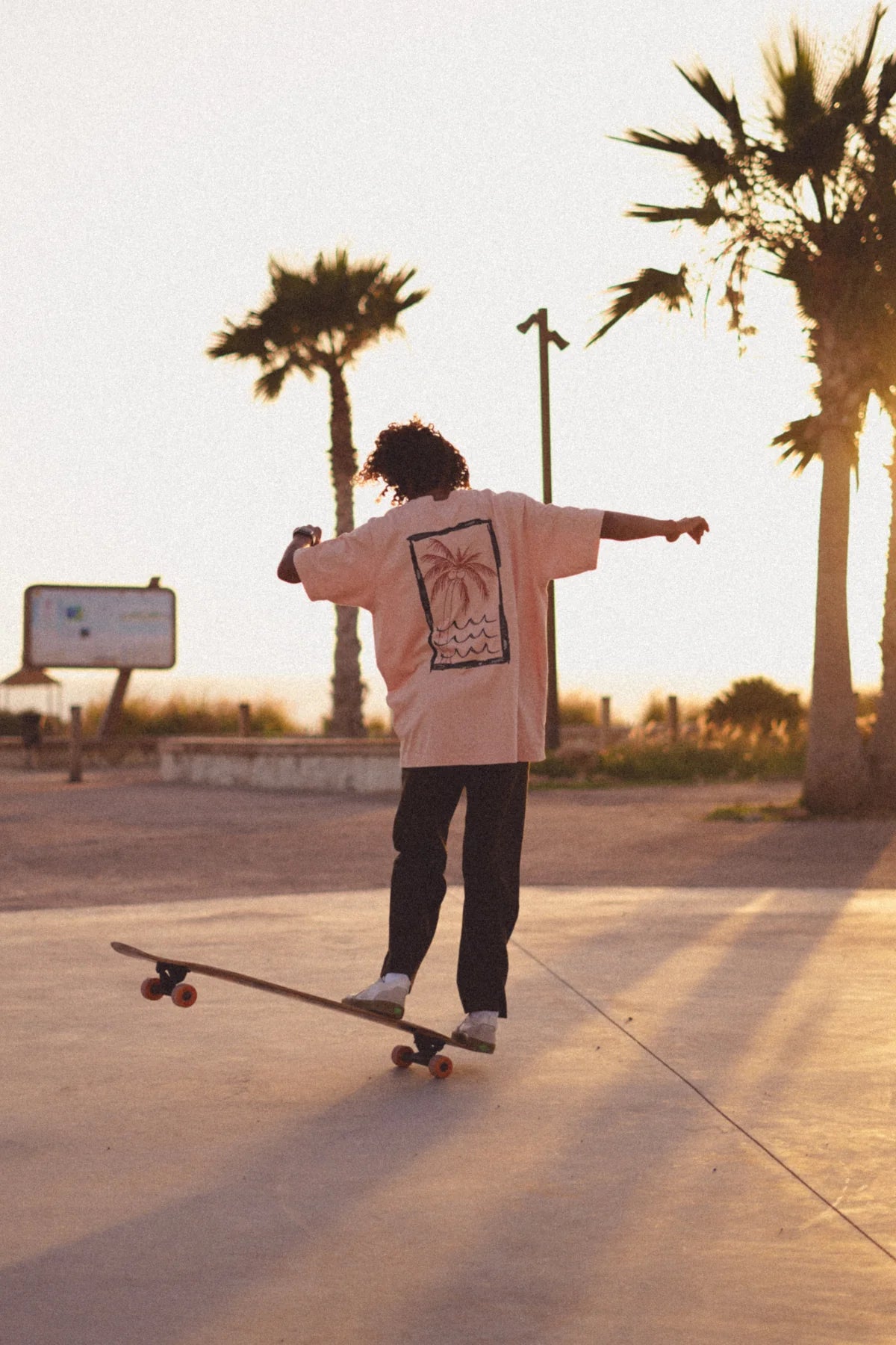 Skater mit korallfarbenem Oversized Shirt von The Sunkissed Rebels von der Seite – Rückprint sichtbar