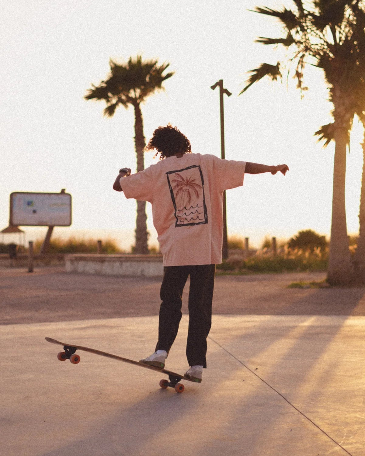 Skater mit korallfarbenem Oversized Shirt von The Sunkissed Rebels von der Seite – Rückprint sichtbar