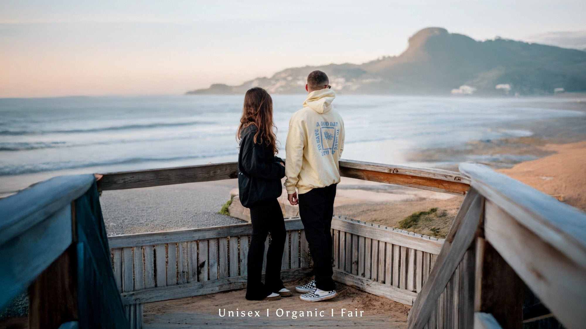 Paar steht am Strand mit gelben Hoodie und schwarzem Sweater von The Sunkissed Rebels