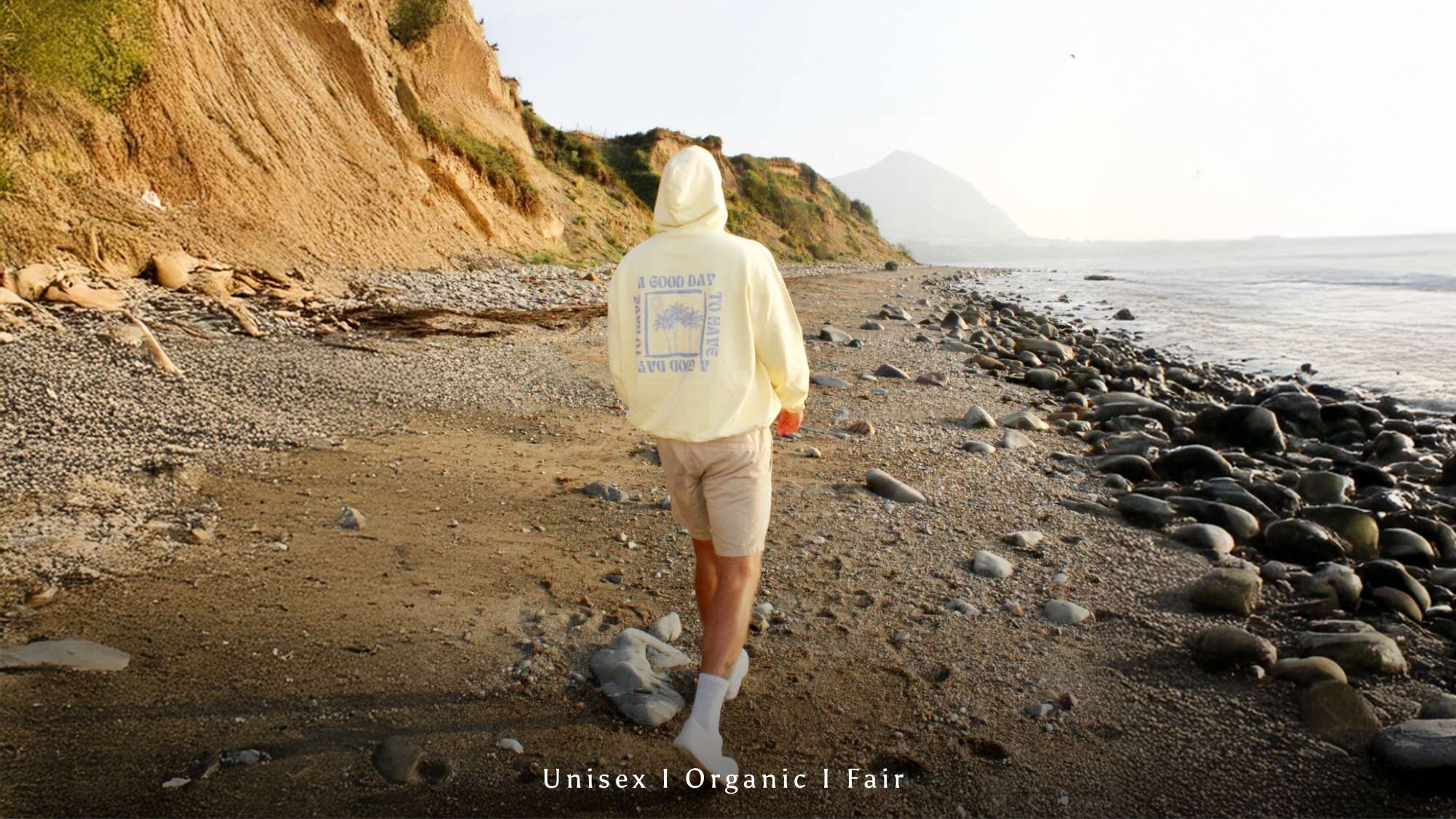 Mann im buttergelbern Hoodie von The sunkissed Rebels läuft am Strand