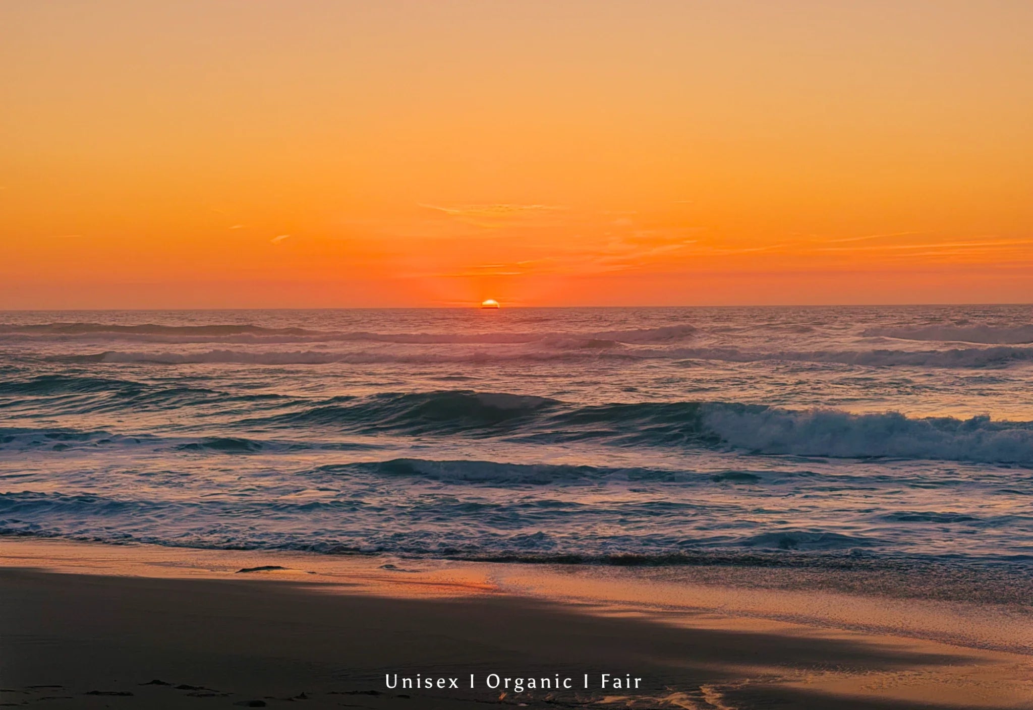 Sonnenuntergang am Strand mit Wellen im Ozean während der Golden Hour, warme orange Farben, ruhige Atmosphäre, nachhaltige Unisex Organic Fair Fashion Ästhetik