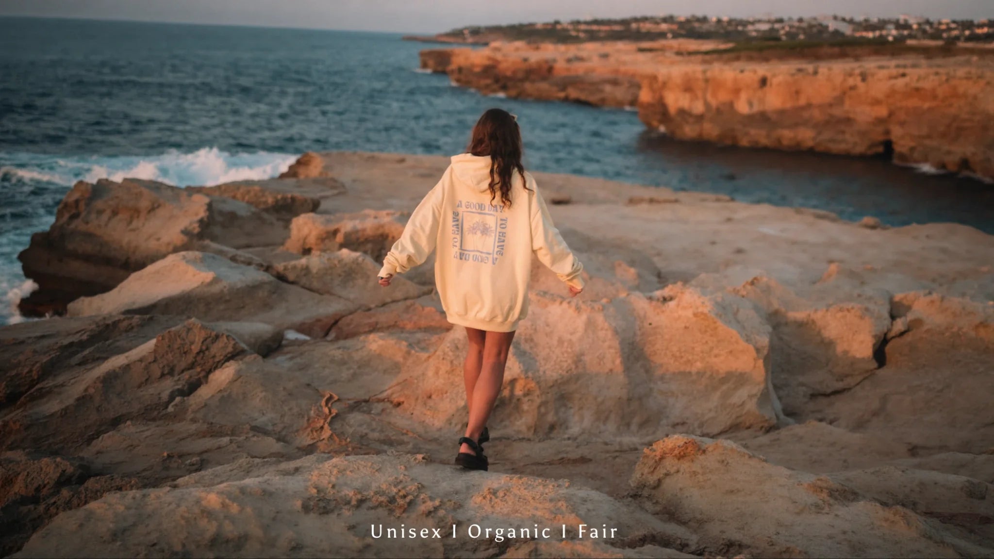 Damen Hoodie der Kollektion „The Sunkissed Rebels“ an einer Felsküste bei Sonnenuntergang – nachhaltige Organic Streetwear für Frauen, fair produziert.