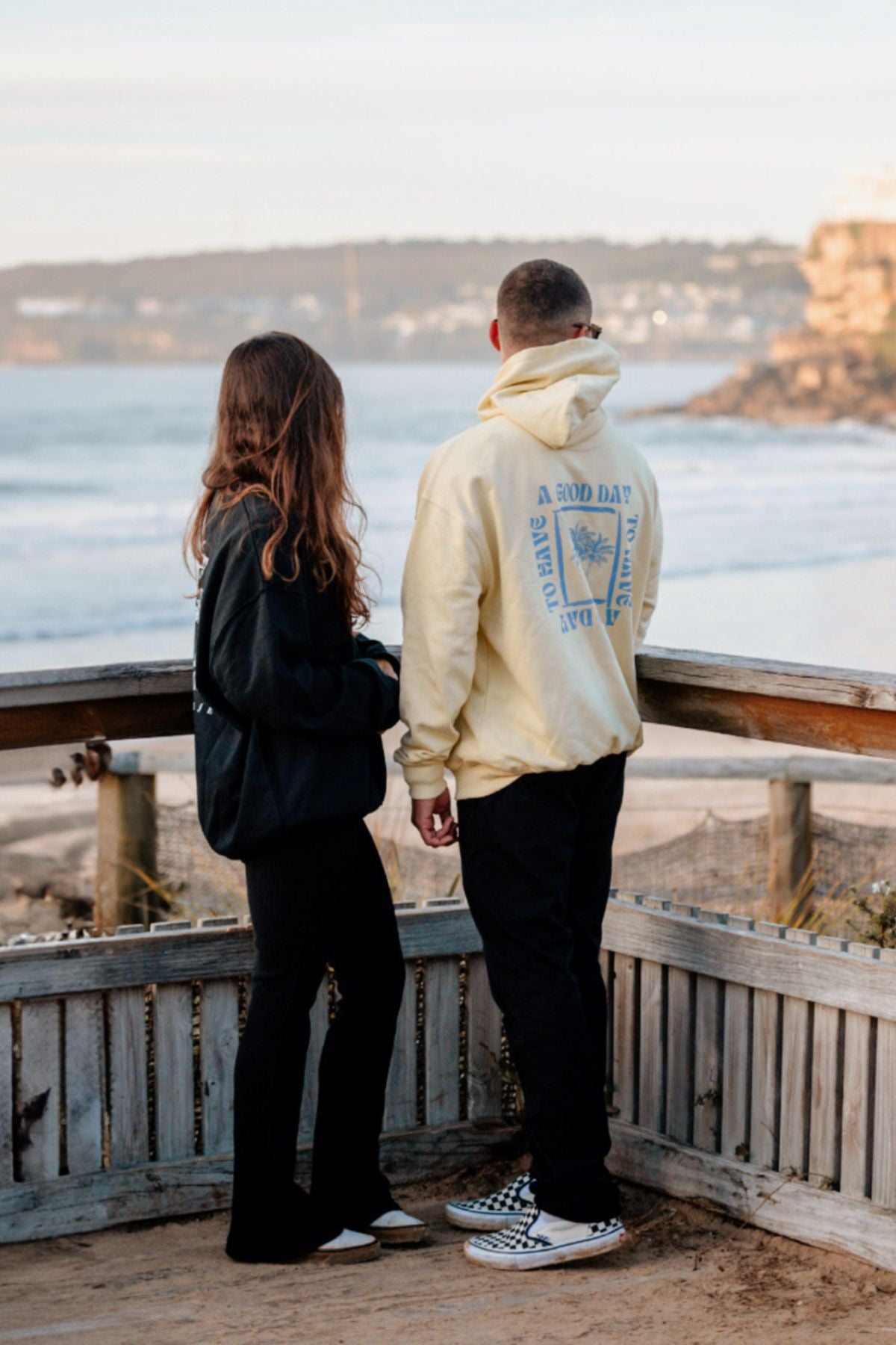 Frau und Man tragen Sweater und Hoodie der A Good Day Kollektion von The Sunkissed Rebels und schauen auf das Meer. 